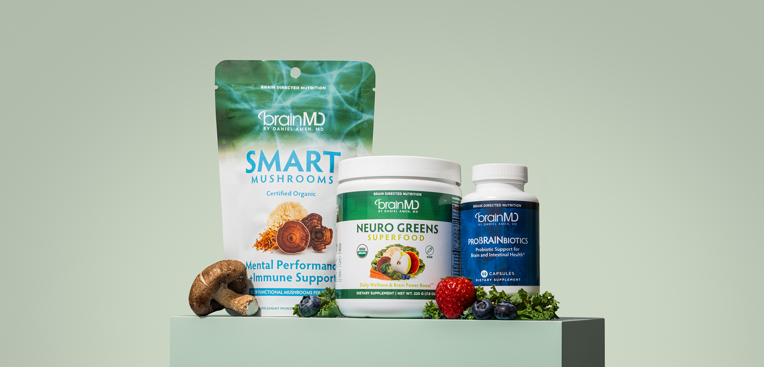 A lineup of dietary supplement products including brainMD Smart Mushrooms, Neuro Greens superfood, and ProBRAINBiotics capsules, surrounded by mushrooms, strawberries, blueberries, and greens.