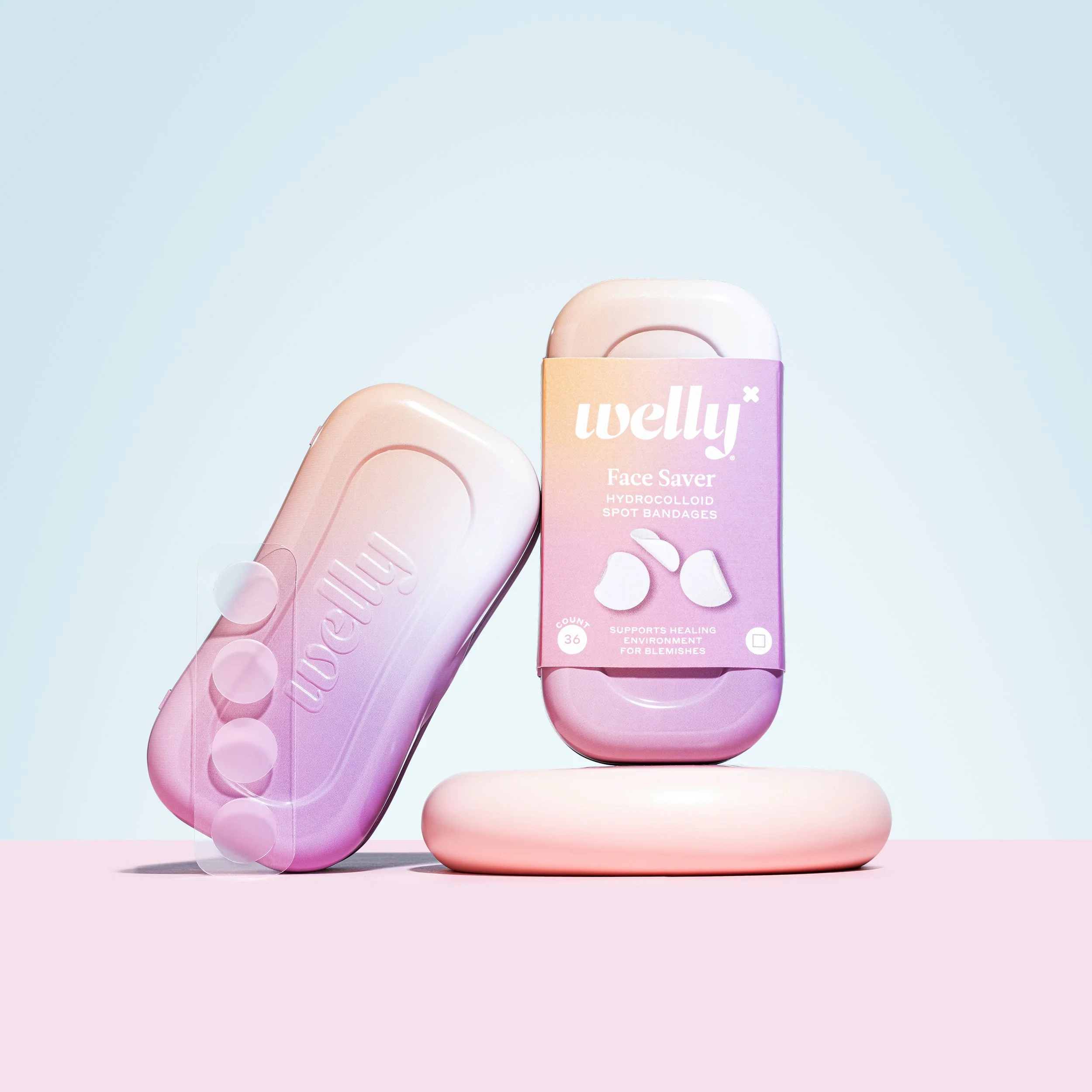 A pink and purple box of Welly Face Saver hydrocolloid spot bandages with 36 bandages inside, placed on a pink surface with a light blue background.