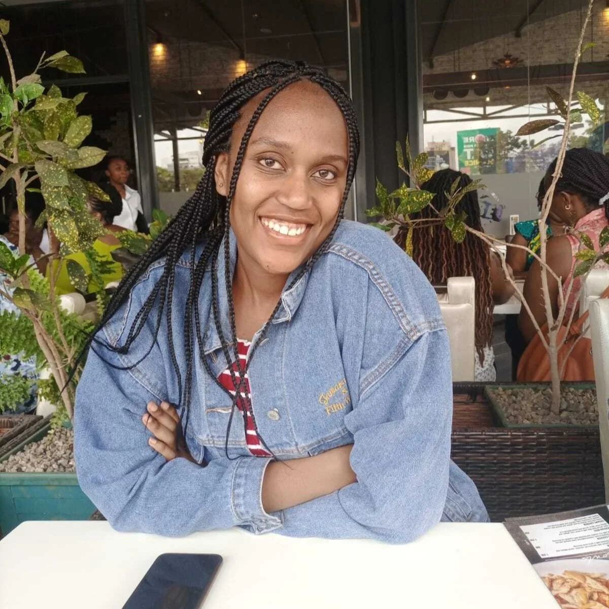 Yvonne is in a restaurant, smiling at the camera with her armed crossed in her denim jacket.