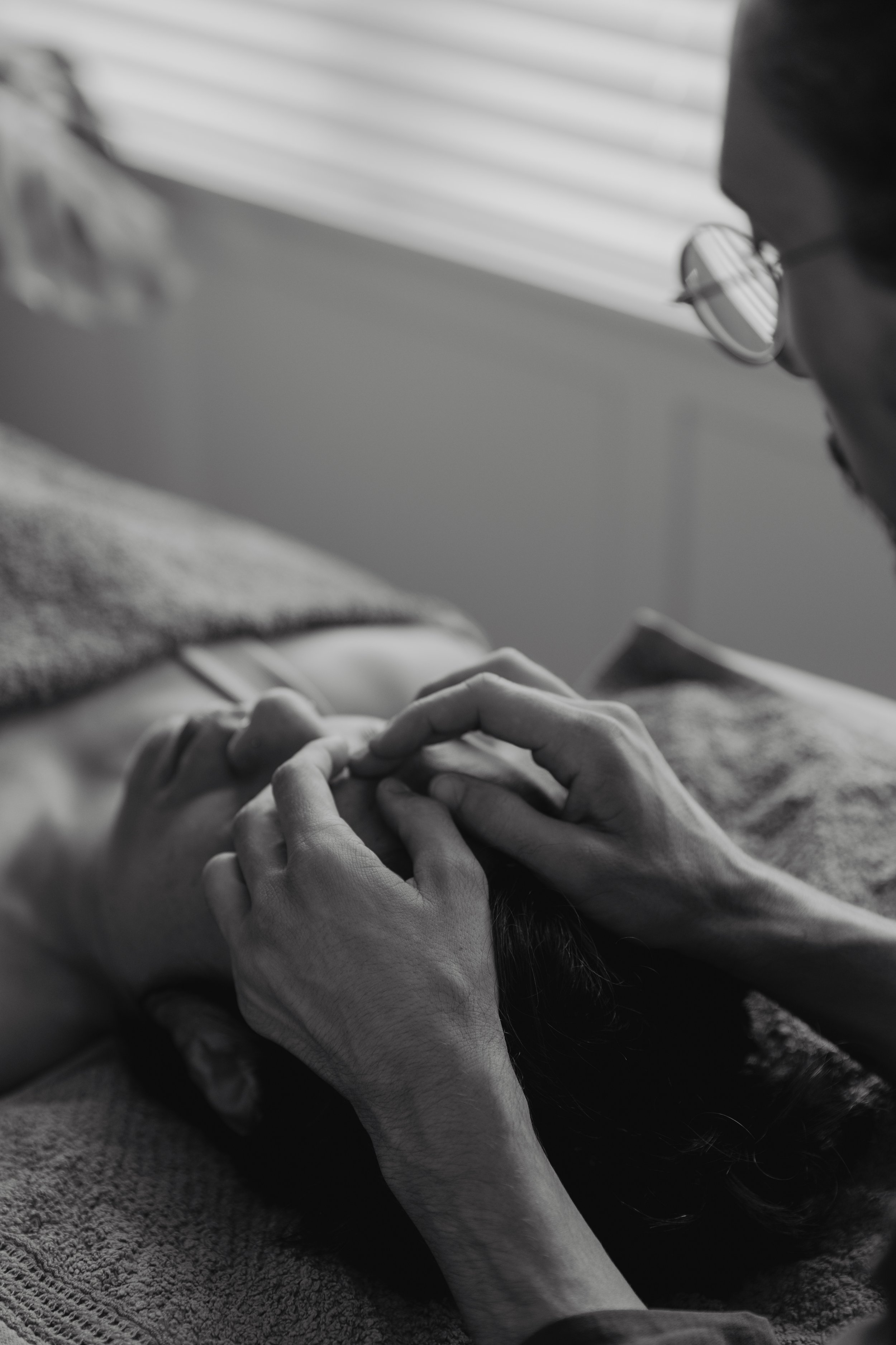 Close-up of Kaspara's hands on a patient's forehead, fingers applying gentle pressure to the frontal bone and supra-orbital ridge during an osteopathic treatment.