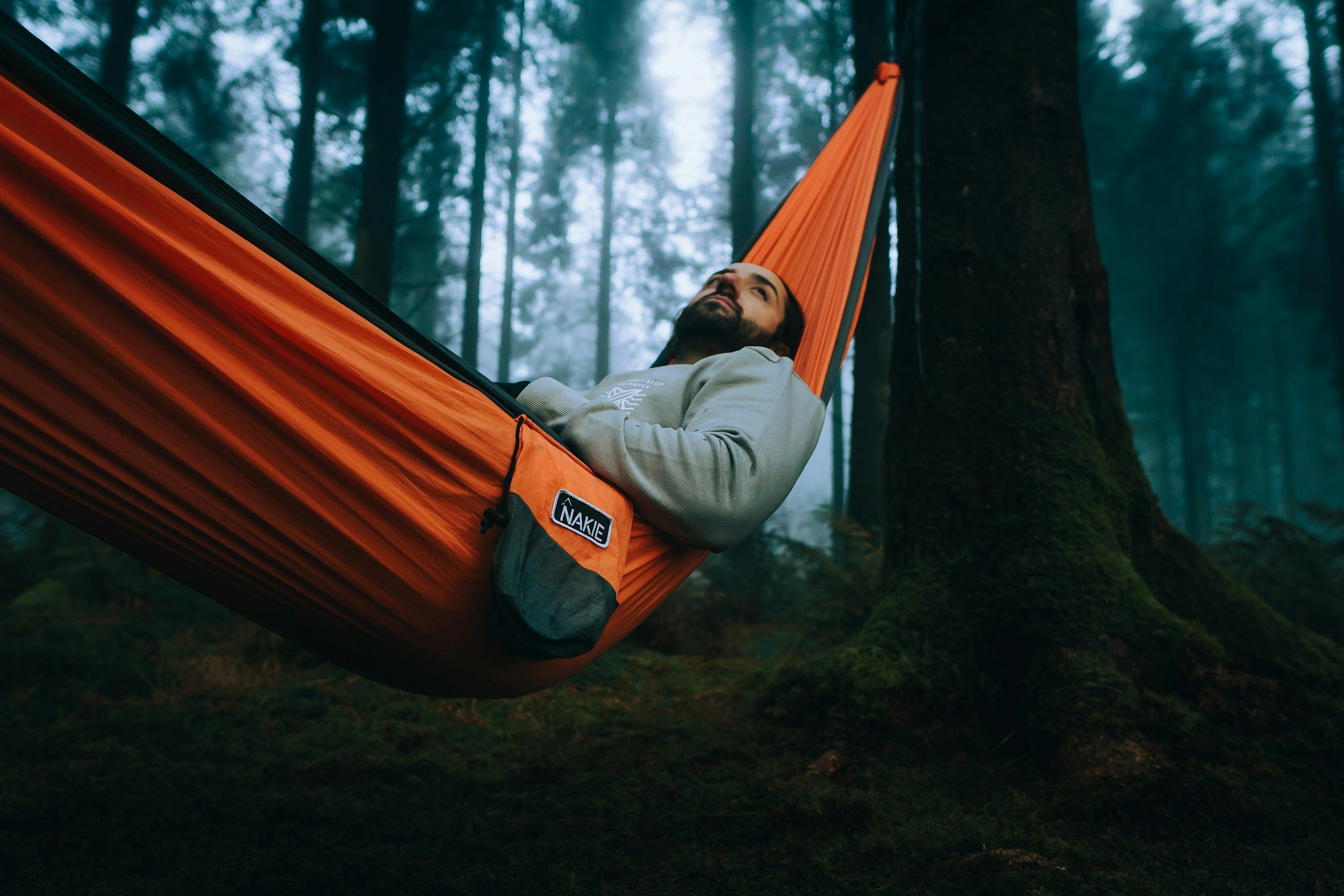 Man relaxing in an orange hammock tied between trees in a misty forest