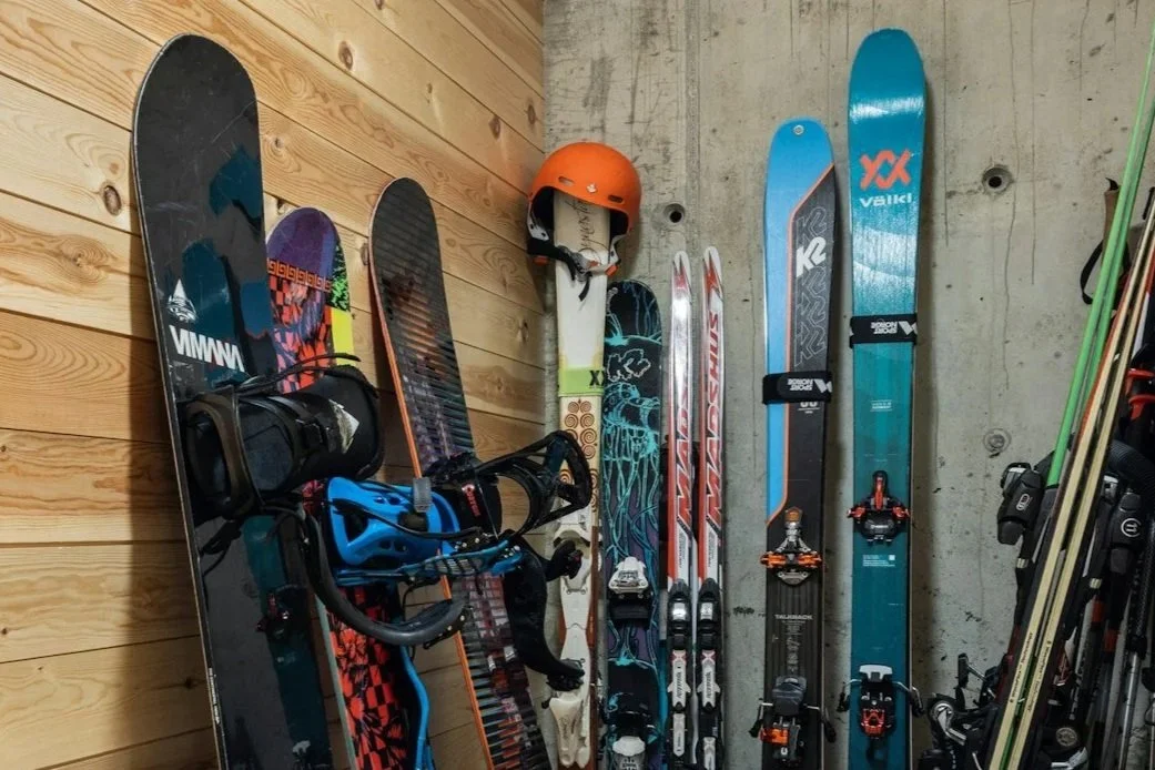 A collection of skis, snowboards, and ski poles stored against a wall in a ski room.