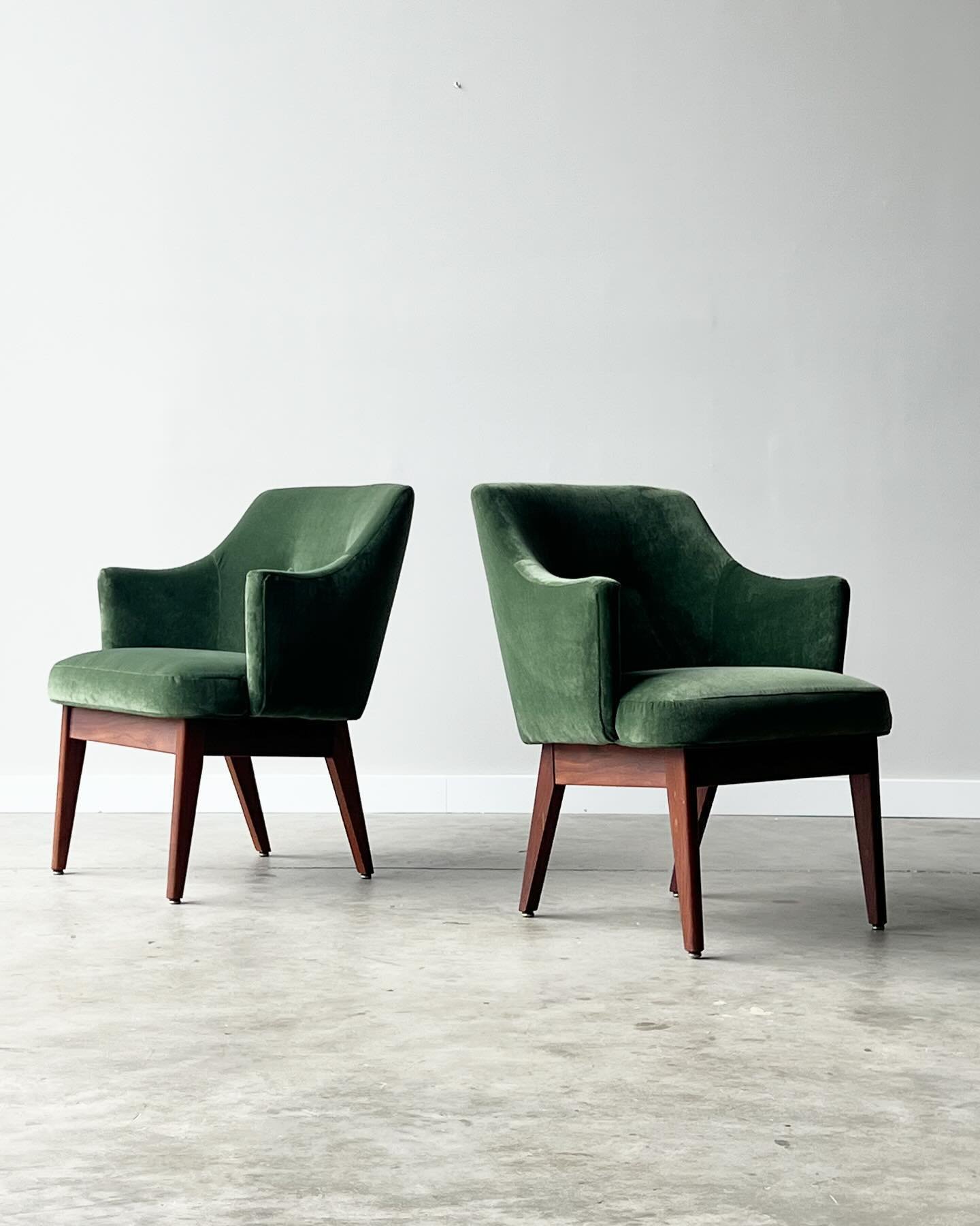 Available ~ Mid-century pair of lounges or accent chairs in the style of Adrian Pearsall. This pair has been newly reupholstered in a forest green soft velvet fabric with two accent buttons on the backrest. They sit on a walnut base with tapered waln