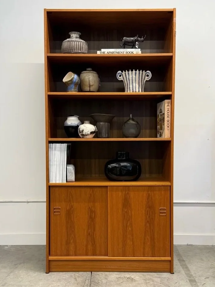 AVAILABLE ~ Mid-century bookshelf made from teak wood, Denmark. Minimalist, yet practical design. This case features three adjustable shelves and four separate levels. Perfect for books, pottery, or whatever you may collect.

The bottom section provi