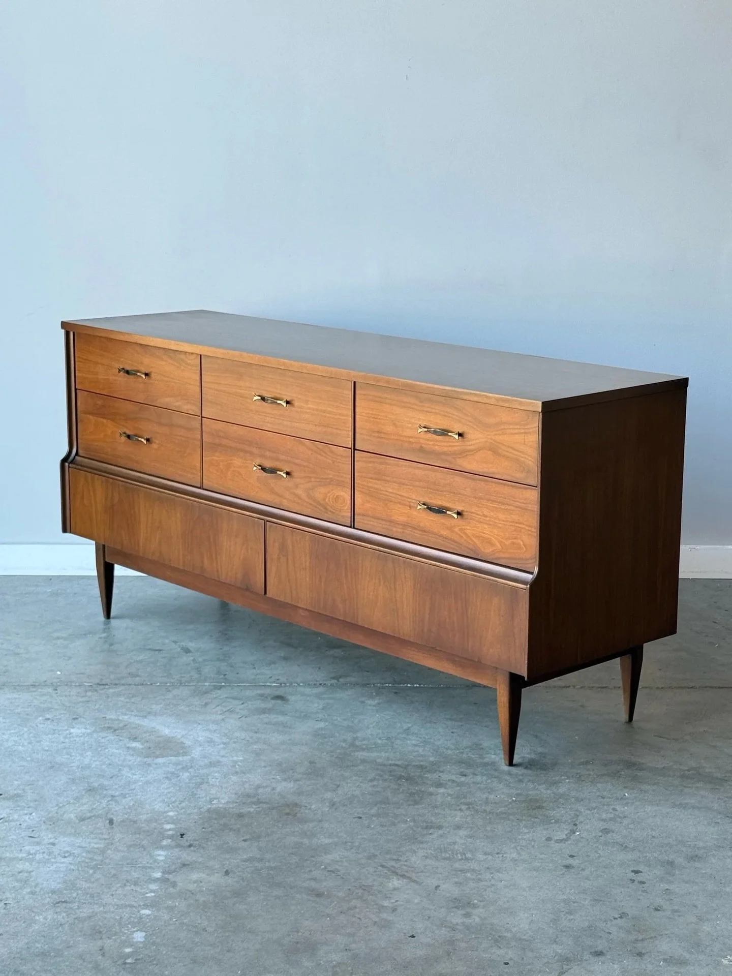AVAILABLE ~ Mid-century eight drawer dresser. Made from walnut wood with a durable laminate top. 

Six drawers align the top stacked in row of two. Each of the top drawers feature the original brass &lsquo;dog-bone&rsquo; pulls. There are two larger 
