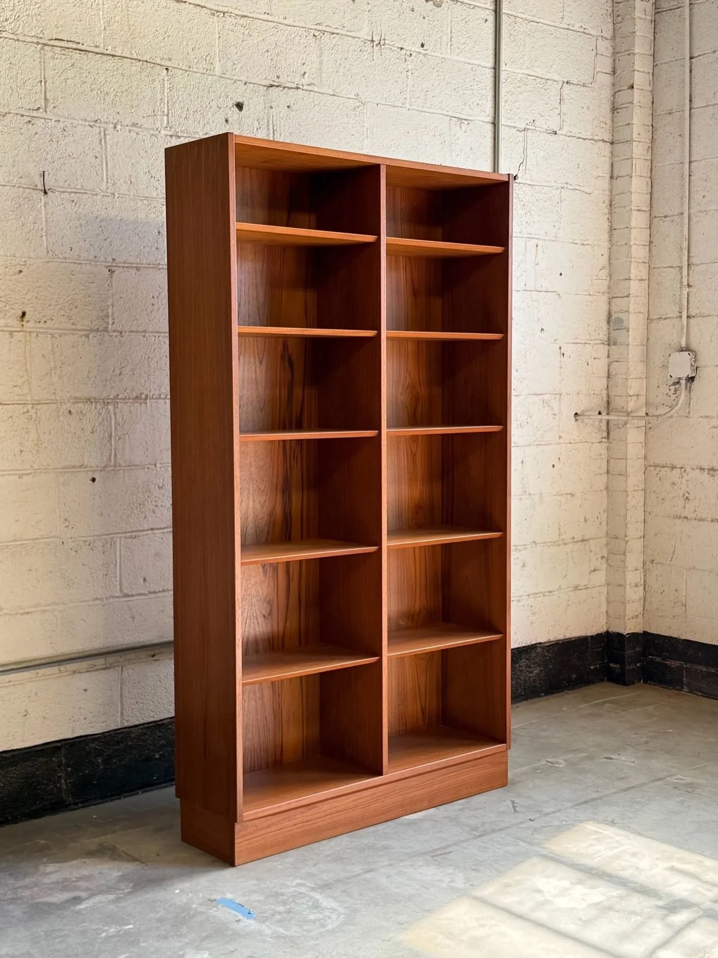 AVAILABLE ~ Mid-century Danish bookshelf by Poul Hundevad and made from teak wood. The teak grain is vibrant and warm. This tall bookshelf features ten shelves, eight of which are adjustable or completely removable. Sitting atop a sturdy teak plinth 