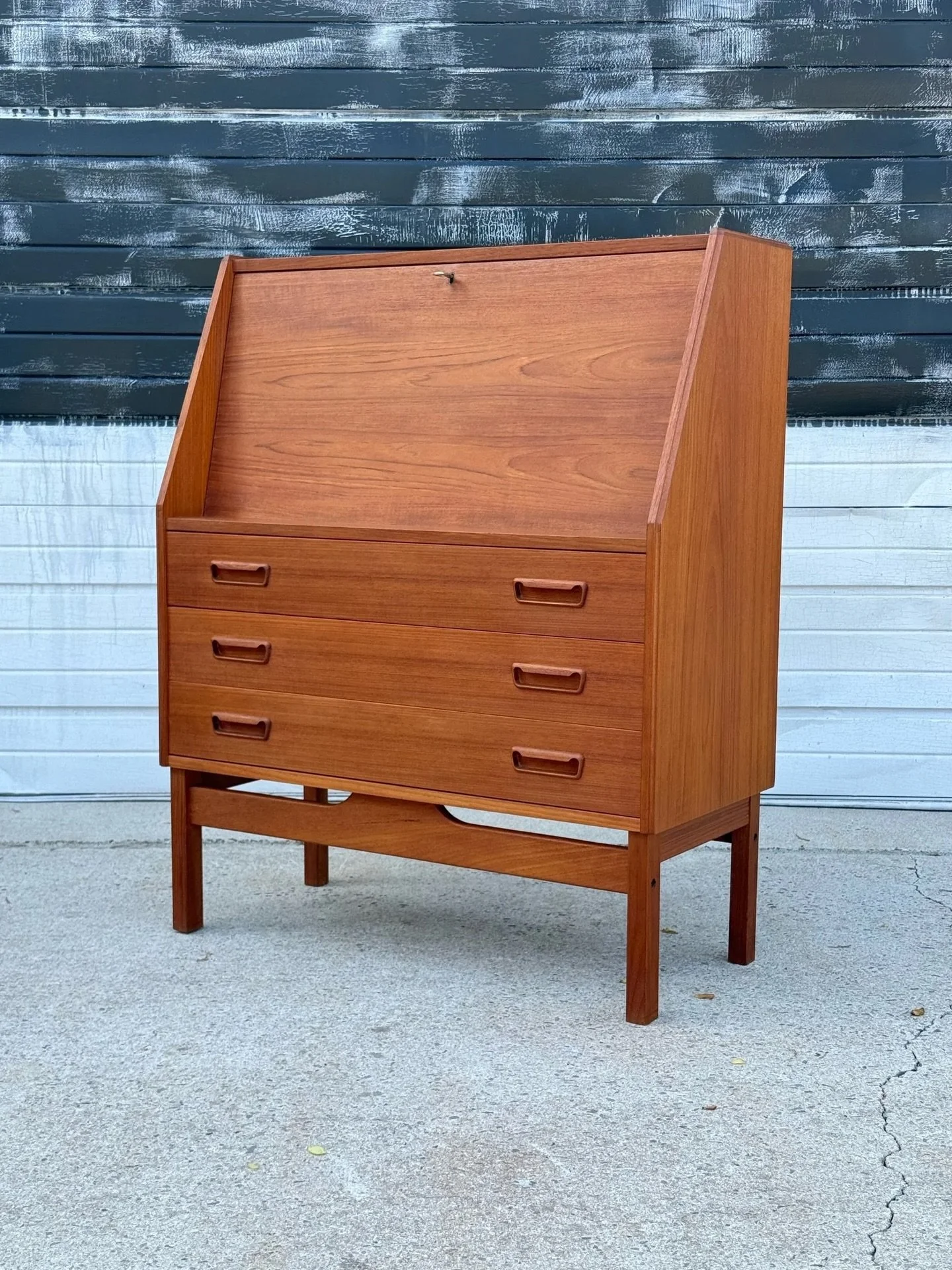 AVAILABLE ~ Mid-century teak secretary desk manufactured by Dyrlund, Denmark. 

Made circa 1960s from teak wood. A gorgeous design with great details. Featuring a bank of three drawers with carved wooden handles. Two handles per drawer that accent th