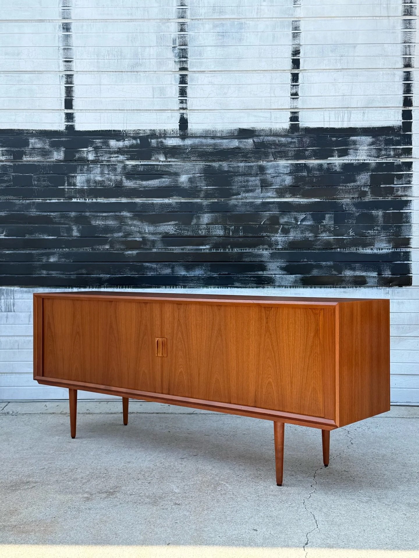 AVAILABLE ~ Mid-century teak credenza designed by Svend Larsen, Denmark. The face of the credenza features two tambour doors that roll back effortlessly with multiple bays of internal storage. Handles are made from carved teak wood and add to the sle