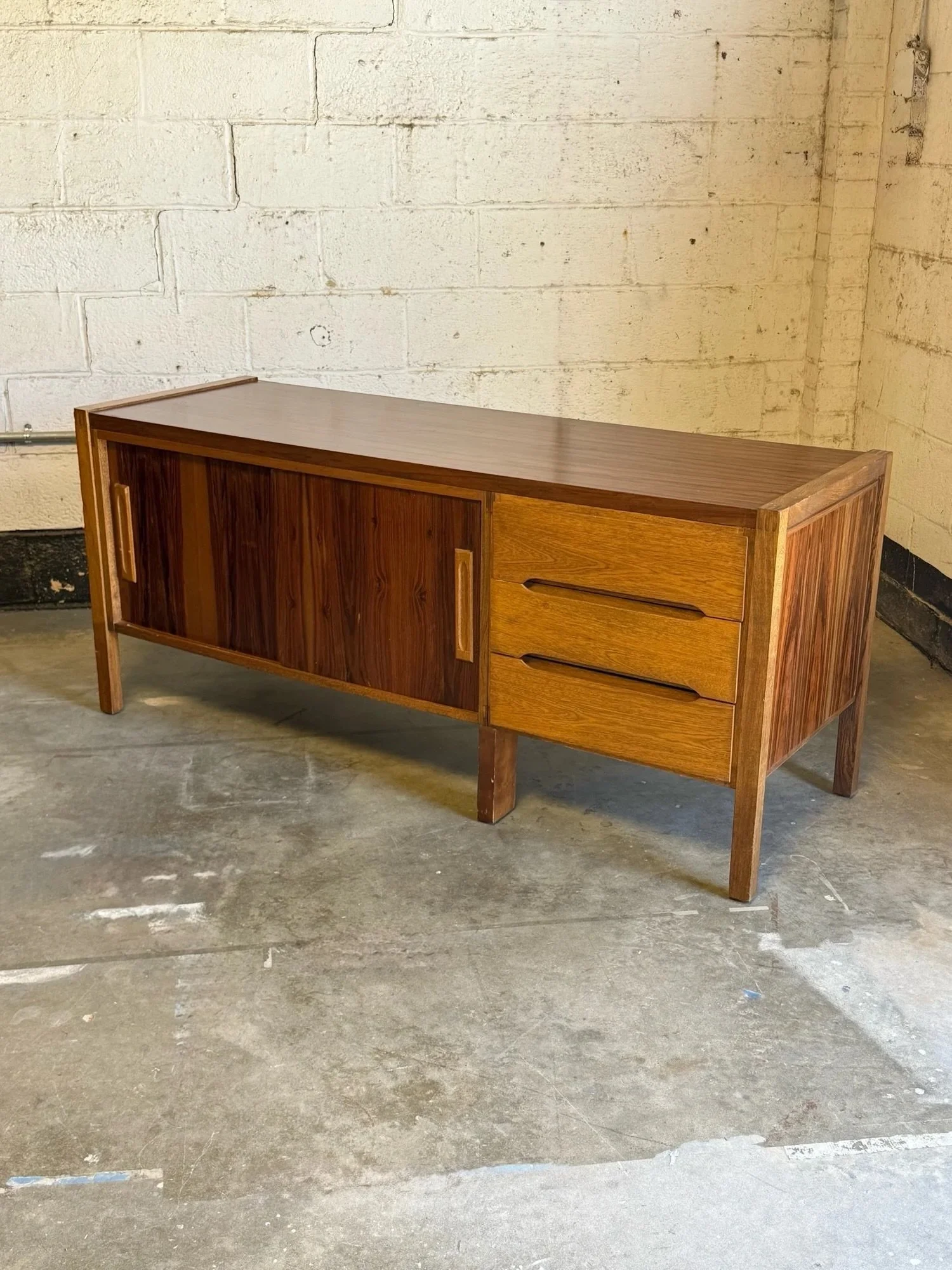 AVAILABLE ~ Mid-century rosewood and palmwood credenza, made in Columbia. This piece features our favorite wood species and incredible wood grain.

The left-hand side has two sliding doors with long oval inset handles. Each door opens to an internal 