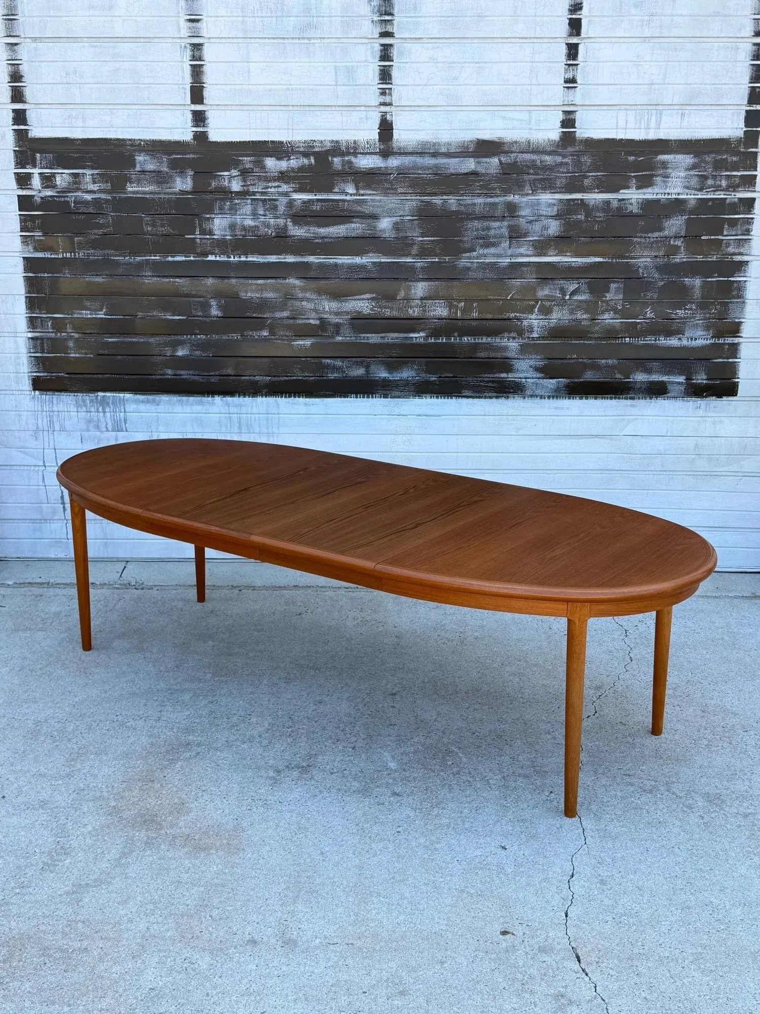 AVAILABLE ~ Mid-century oval expanding dining table. Made from teak wood, Denmark. The table top is oval in shape with thick rounded edges and lower support skirt. Vibrant teak woodgrain throughout the top.

Equipped with two removable leaves and int