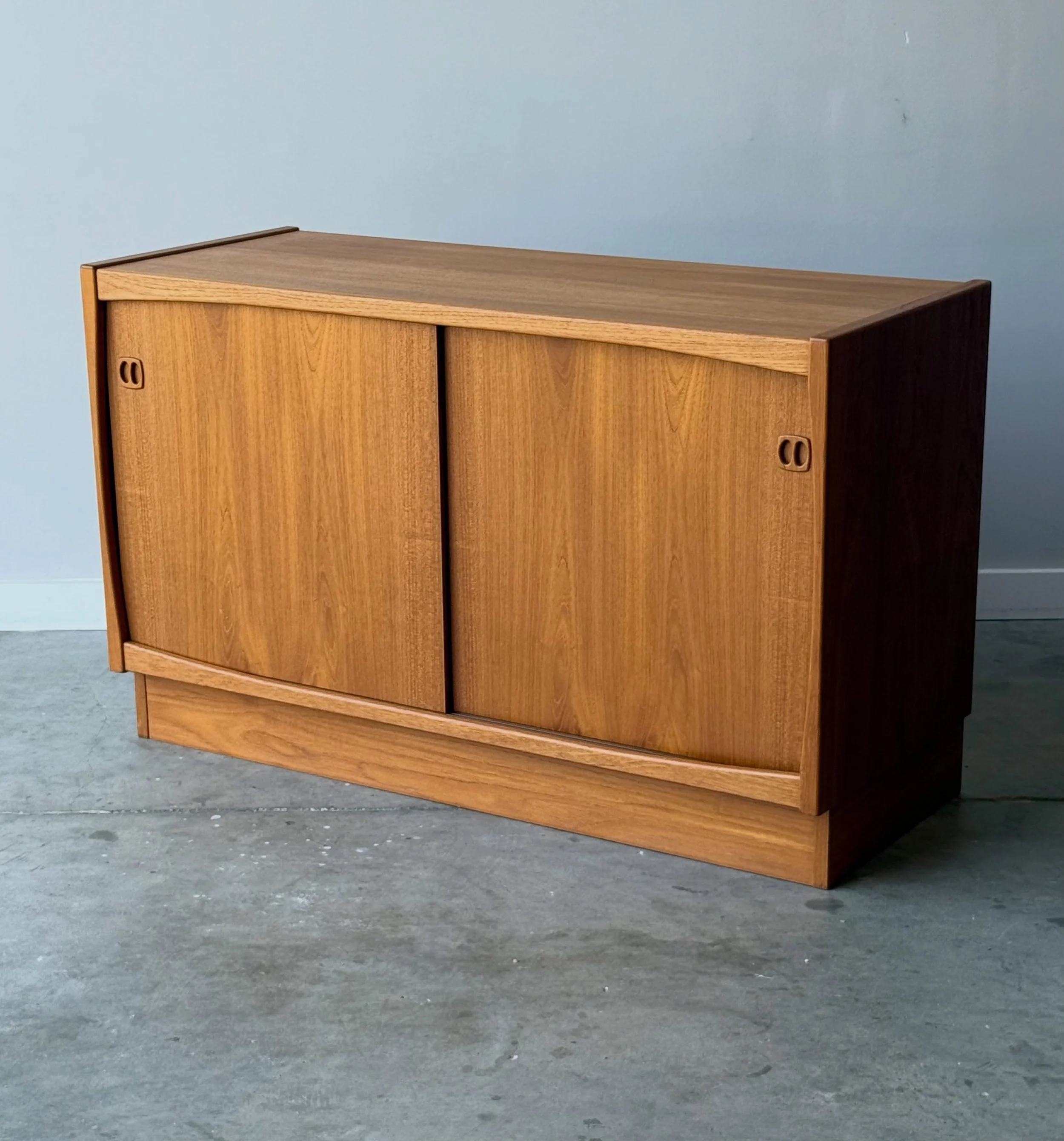AVAILABLE ~ Mid-century credenza designed by Laurtis and Larsen, Denmark. This small-scale credenza is made from teak wood. Excellent teak grain throughout the entire credenza. 

Featuring two smooth sliding doors aligning the front. The handles for 