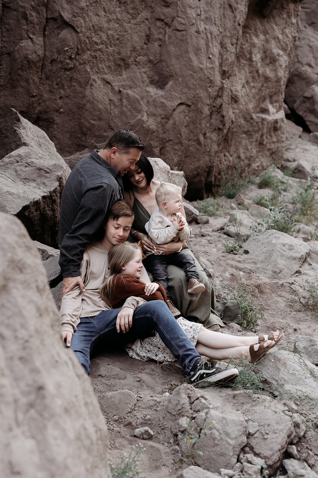 Southern California family photographer captures family in the rocky desert near Palm Springs California. Family holds each other on a pile of rocks in painted canyon