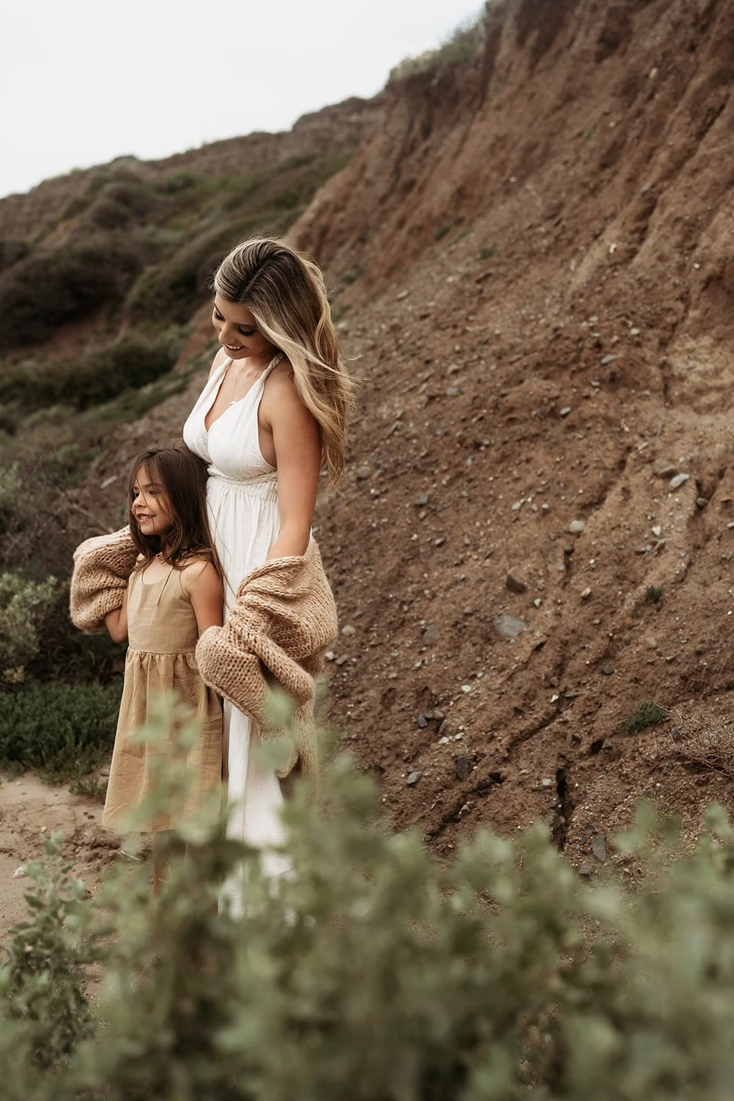 Southern California family photographer captures family on the rocky beach near san Clemente California. Mother holds her daughter and looks out at the water