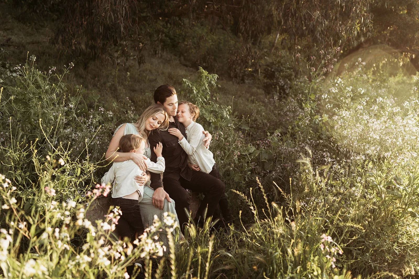 Southern California family photographer captures family in this rich, moody edit at gum grove park near Long Beach California. family is cuddling in the flowers while sitting on a log