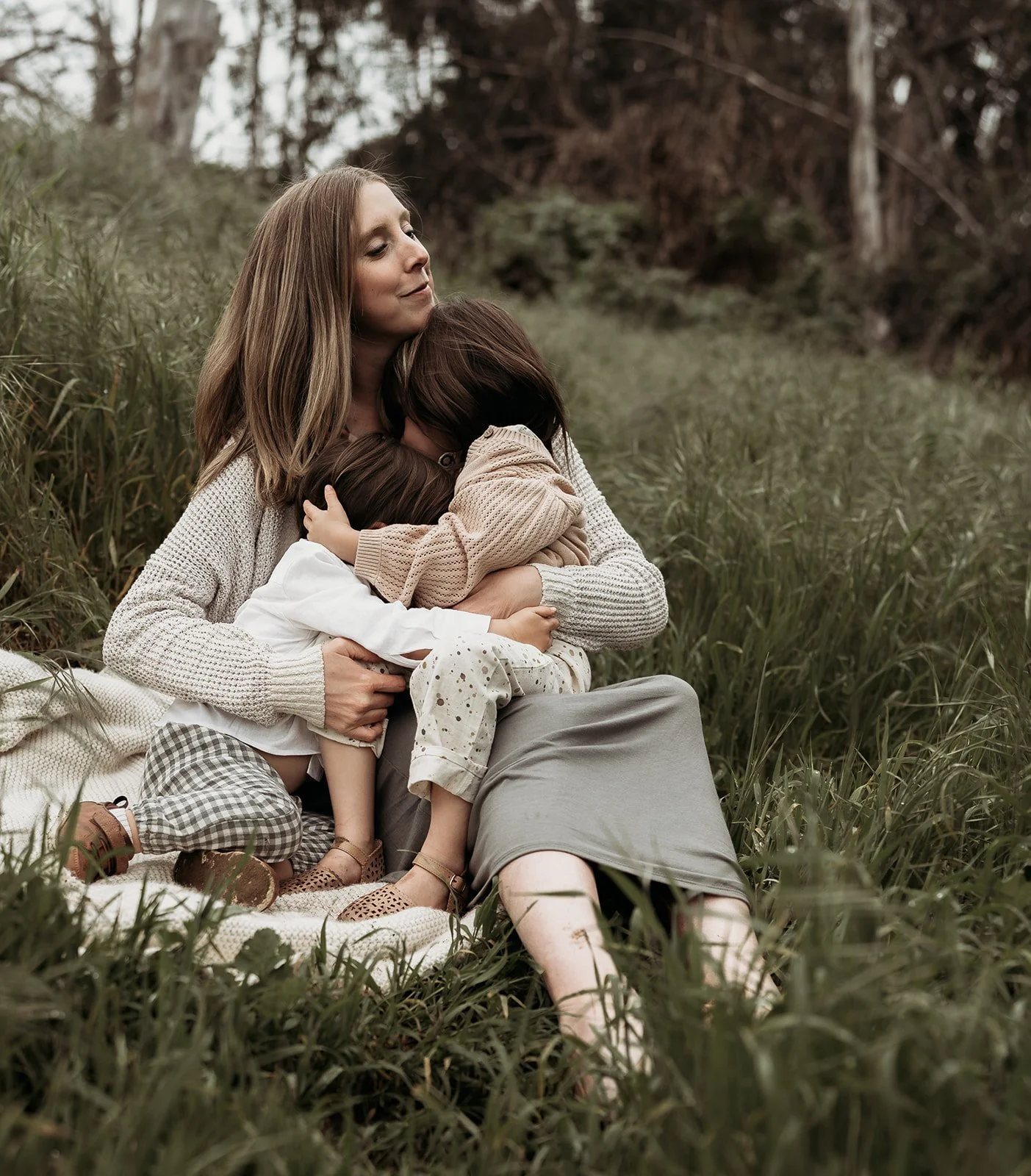Southern California family photographer captures mother holding her two children in the grassy hills of frog creek park in Long Beach California.