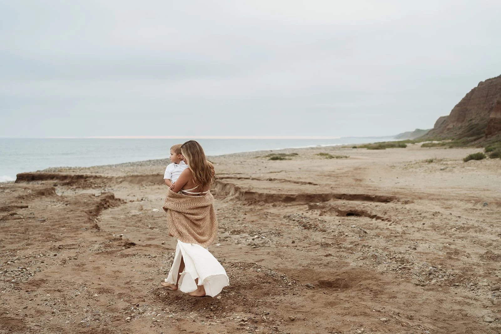 Southern California family photographer captures family on the rocky beach near san Clemente California. Mother holds her son and looks out at the water