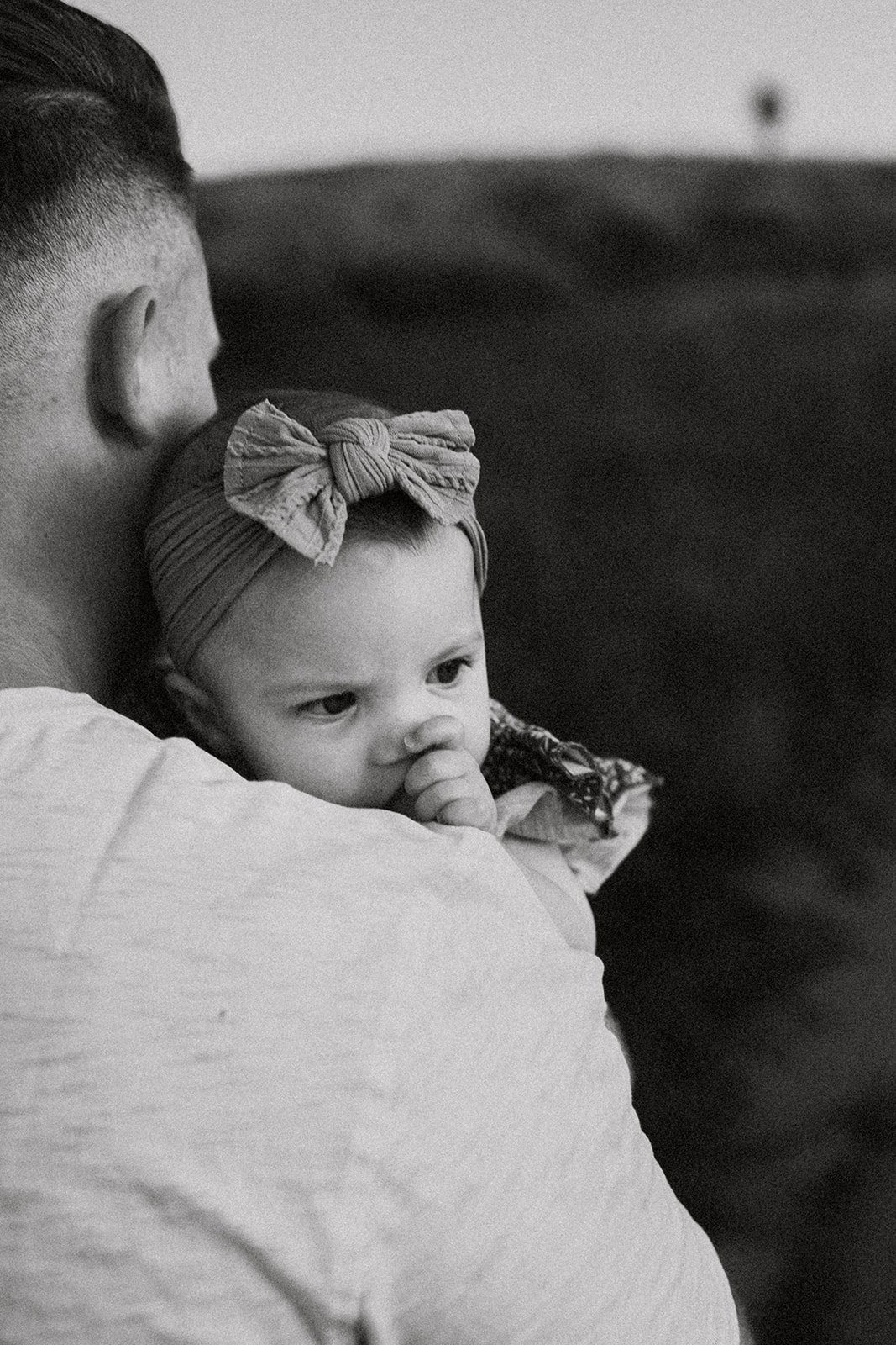 Southern California family photographer captures dad carrying daughter through sycamore creek park in riverside California. daughter is sucking her thumb as they walk in the sunset.