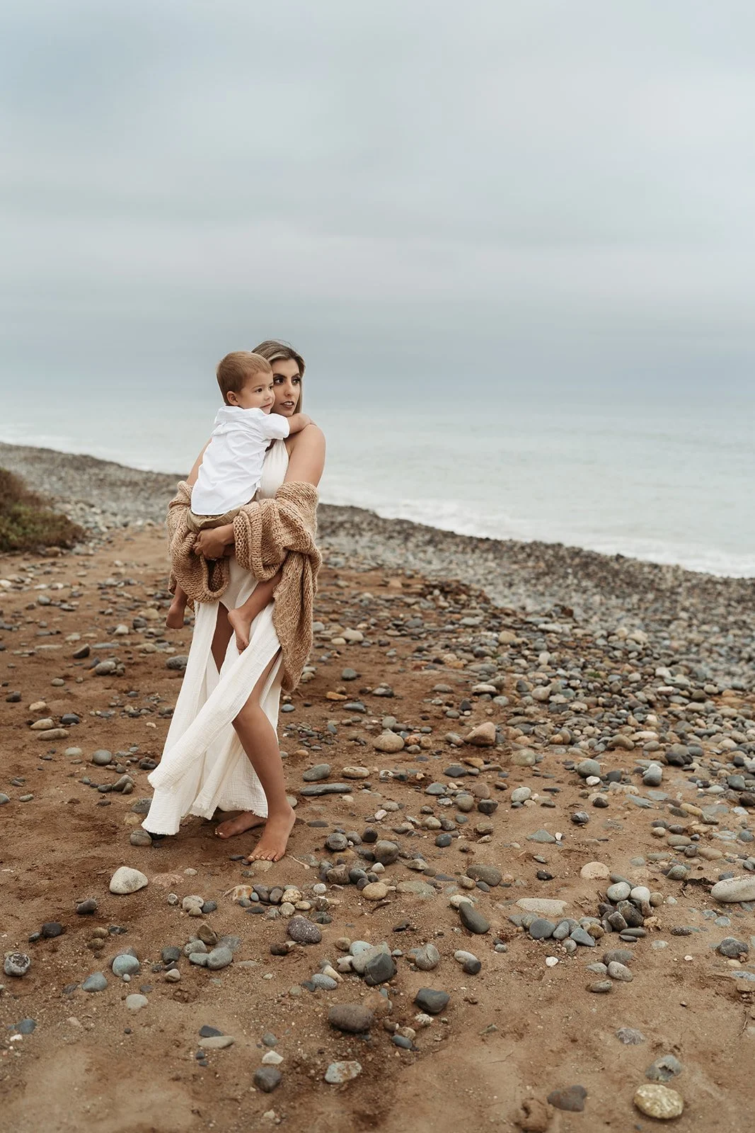 Southern California family photographer captures family on the rocky beach near san Clemente California. Mother holds her son and looks out at the water