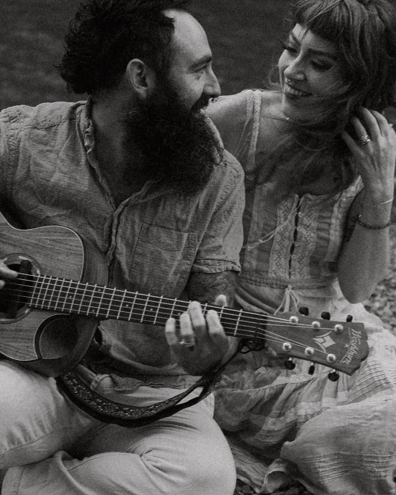 Glacier National Park Elopement photographer captures couple playing guitar and snuggling near two medicine lake, Montana. couple is wearing brown dress and blue linen outfit