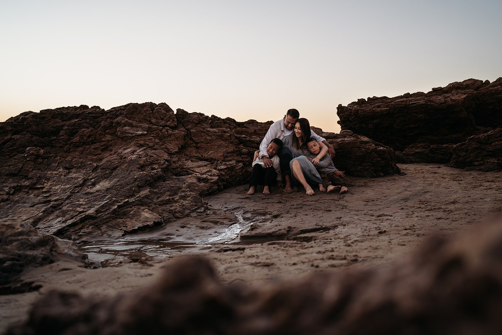 Southern California family photographer captures family snuggling on the beach in Newport Beach California. moody rich brown edit