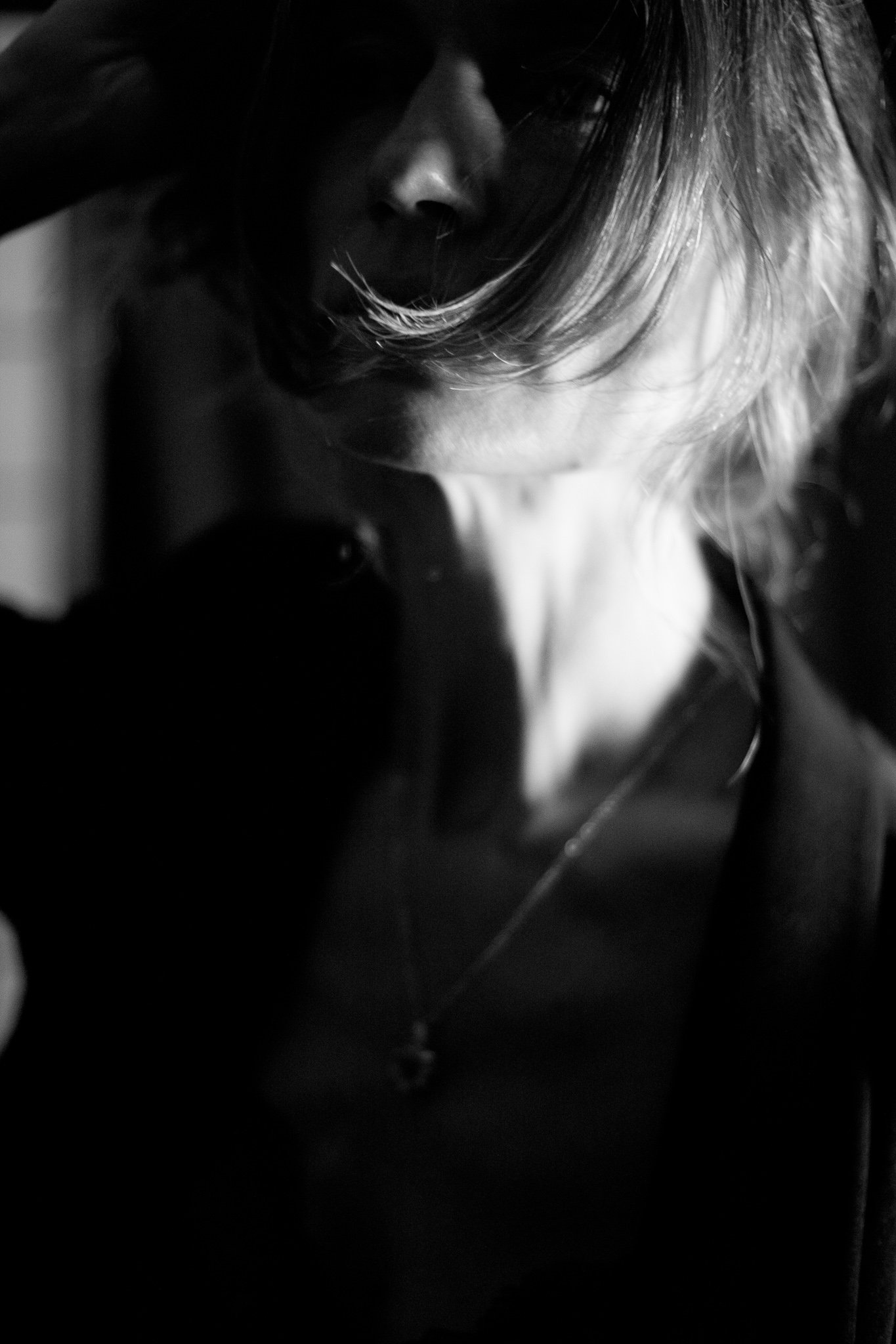 Black and white close-up portrait of a woman with her face partially obscured, looking downward, with tousled hair covering part of her face.