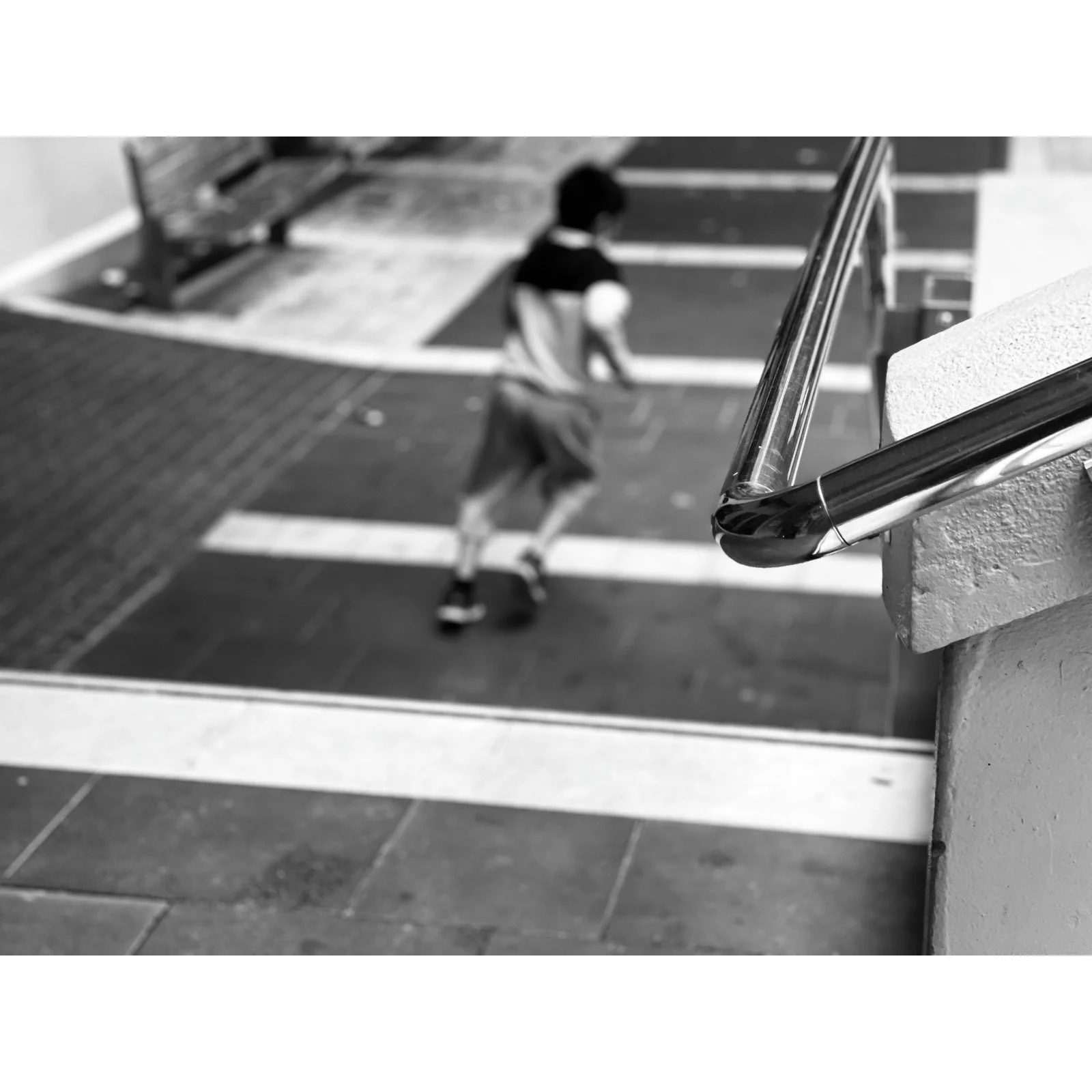 Blurred boy skateboarding on a sidewalk near a staircase with a chrome handrail in black and white.