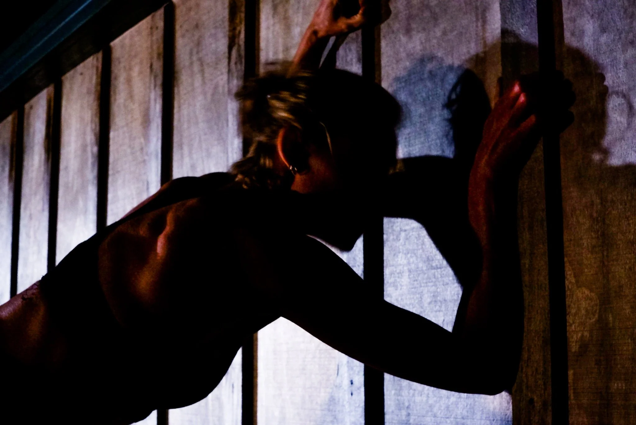 Silhouette of a person leaning against a wooden wall, with their head bowed and hand pressed against the wall, in low lighting.