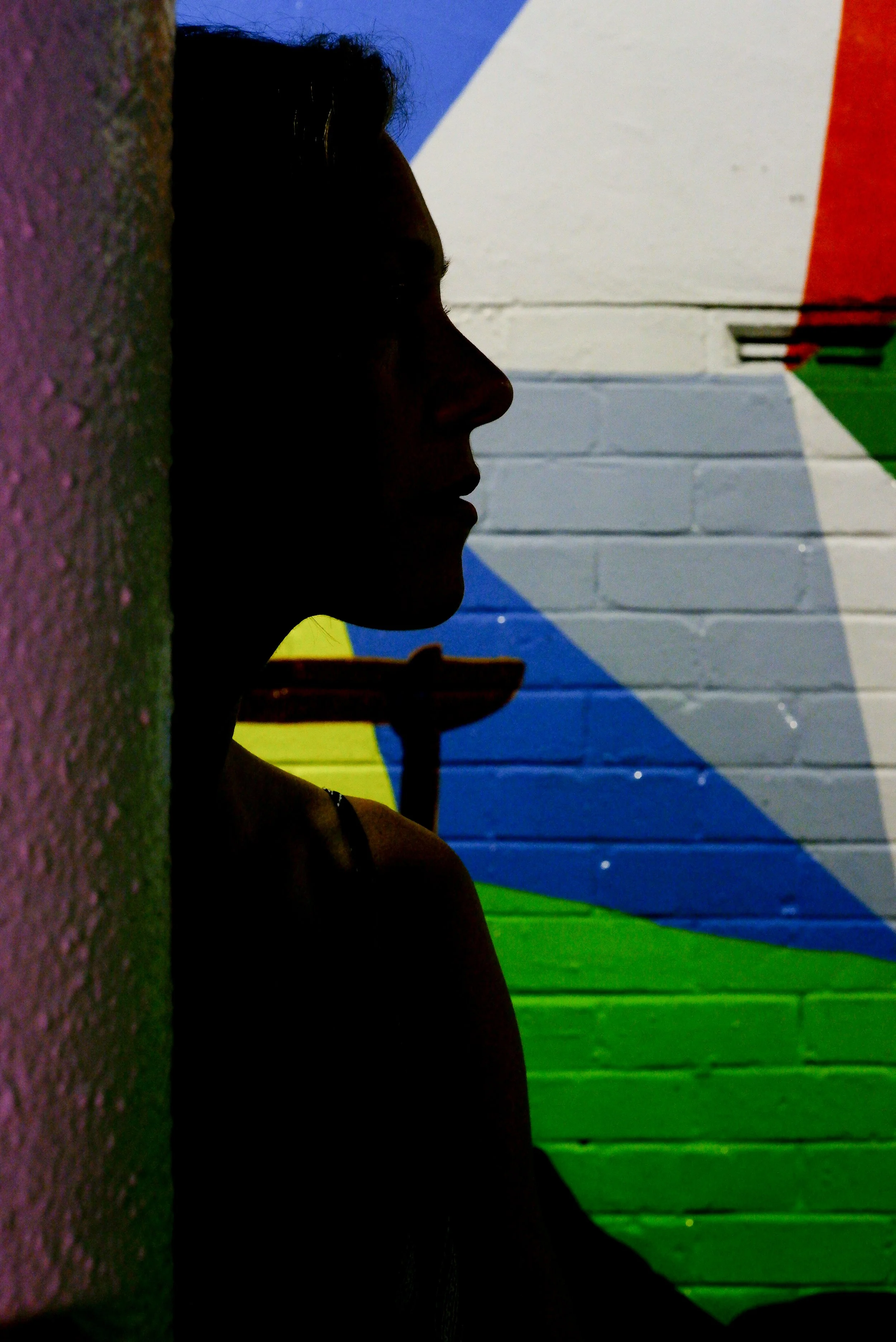 Silhouette of a person leaning against a wall with colorful mural featuring abstract shapes and vibrant colors in the background.