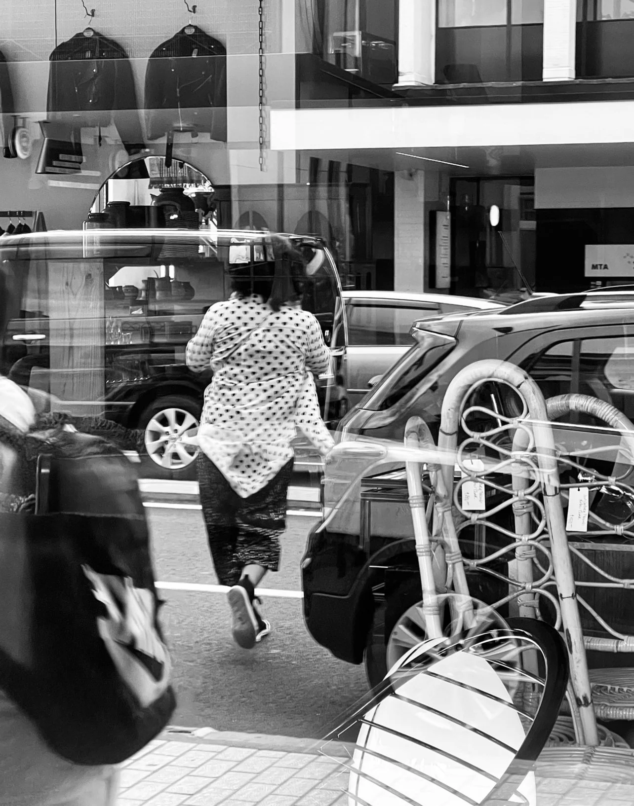 Reflection of a city street scene through a glass window, showing a person running and various parked cars and furniture outside.