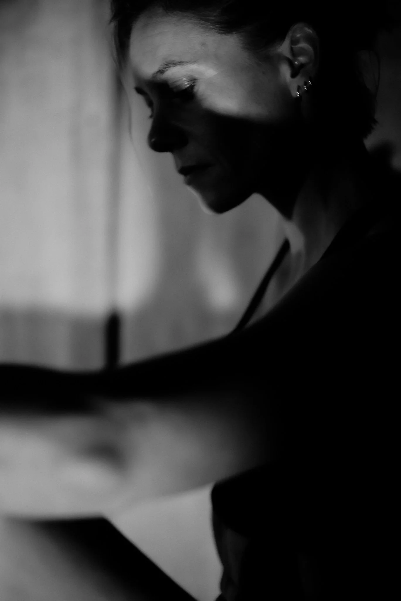 A black and white photo of a woman with short hair and earrings, looking downward with a contemplative expression.