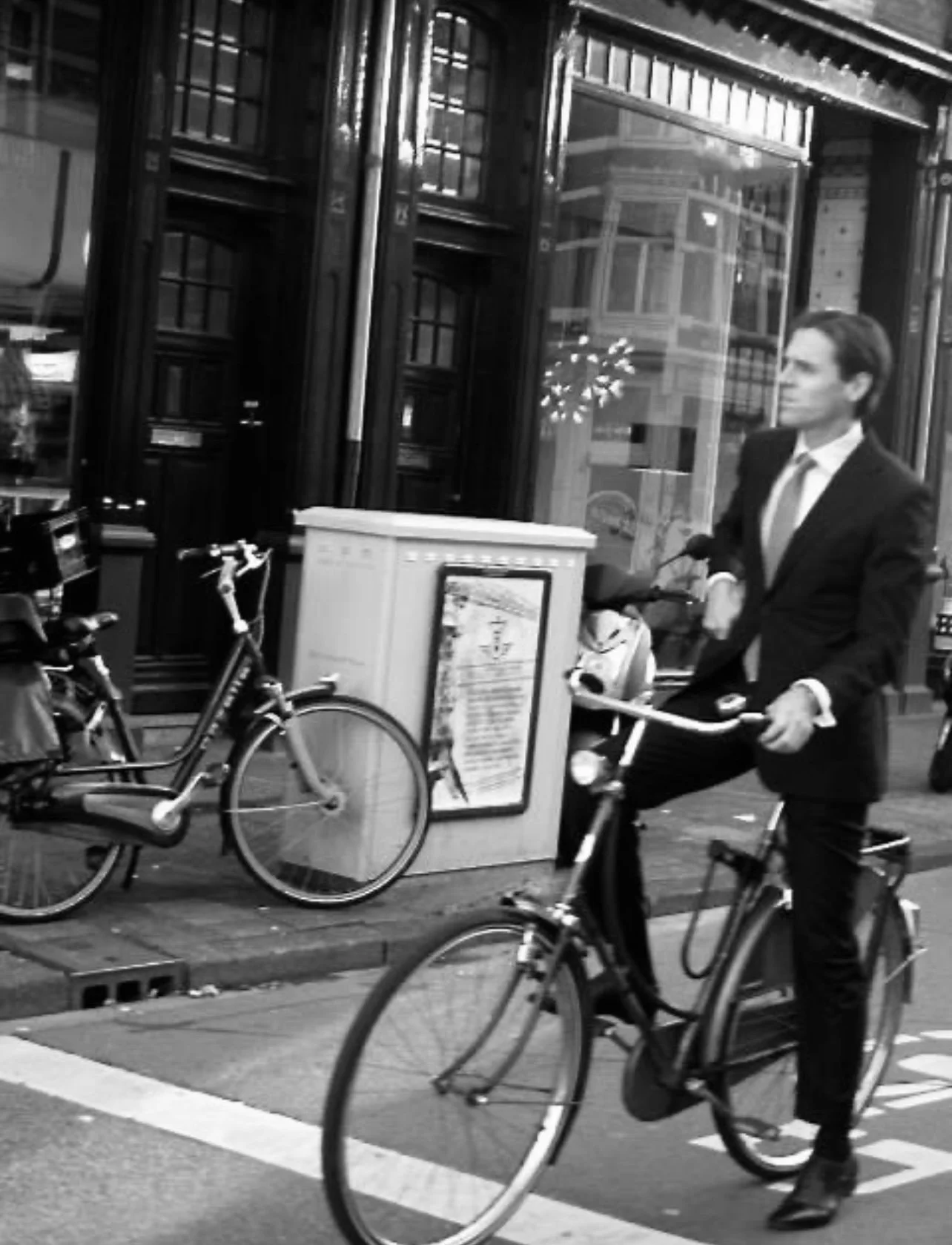 A man in a business suit riding a bicycle on the city street.