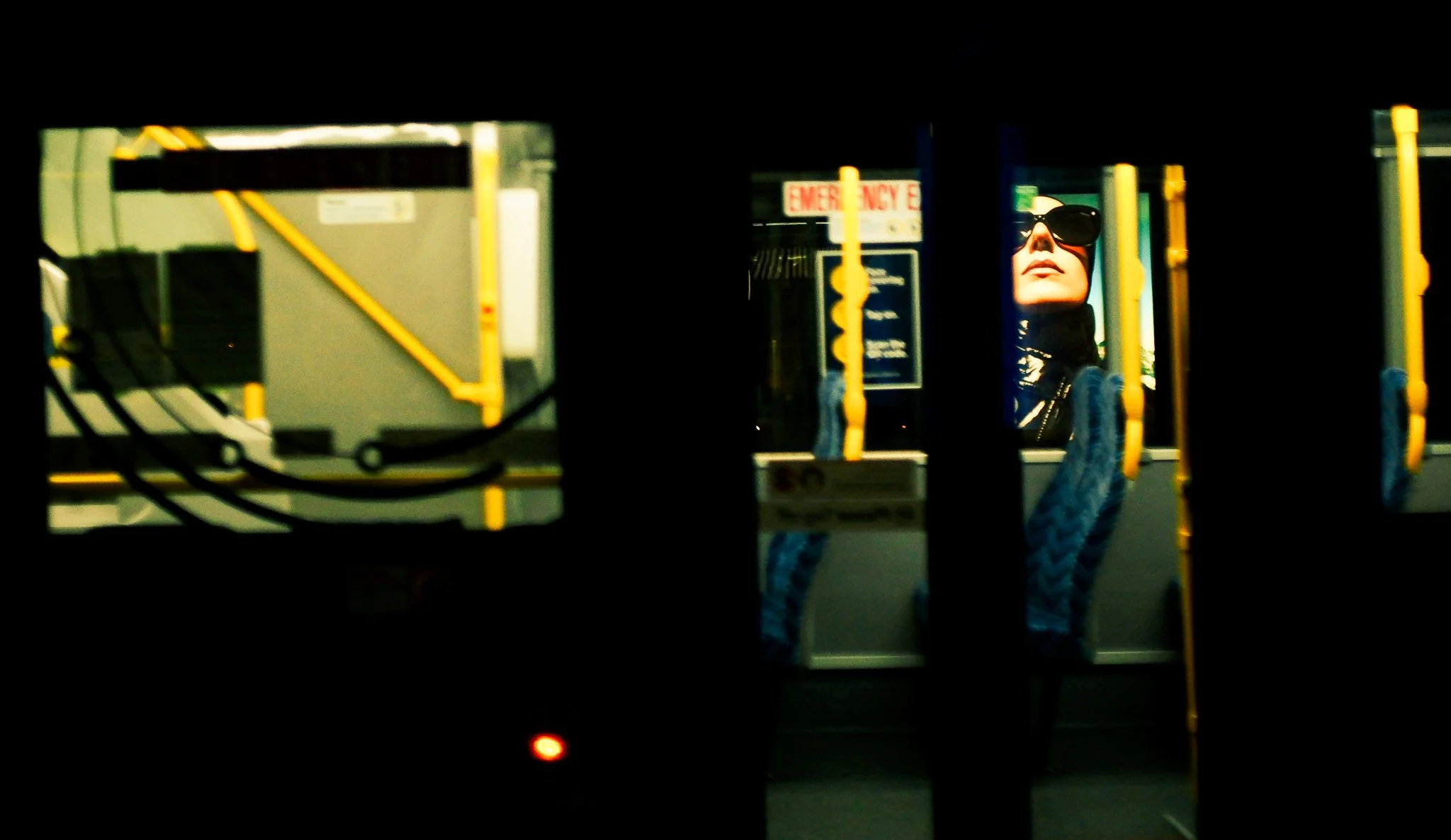 Woman with sunglasses sitting in a bus or train, seen through a partially open door or window.