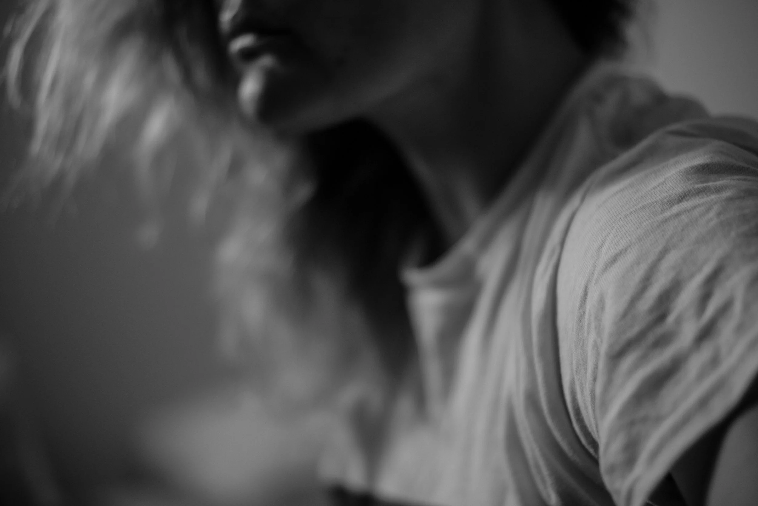 A black and white close-up photo of two people kissing, focused on their faces and lips, with one person's face partially visible.