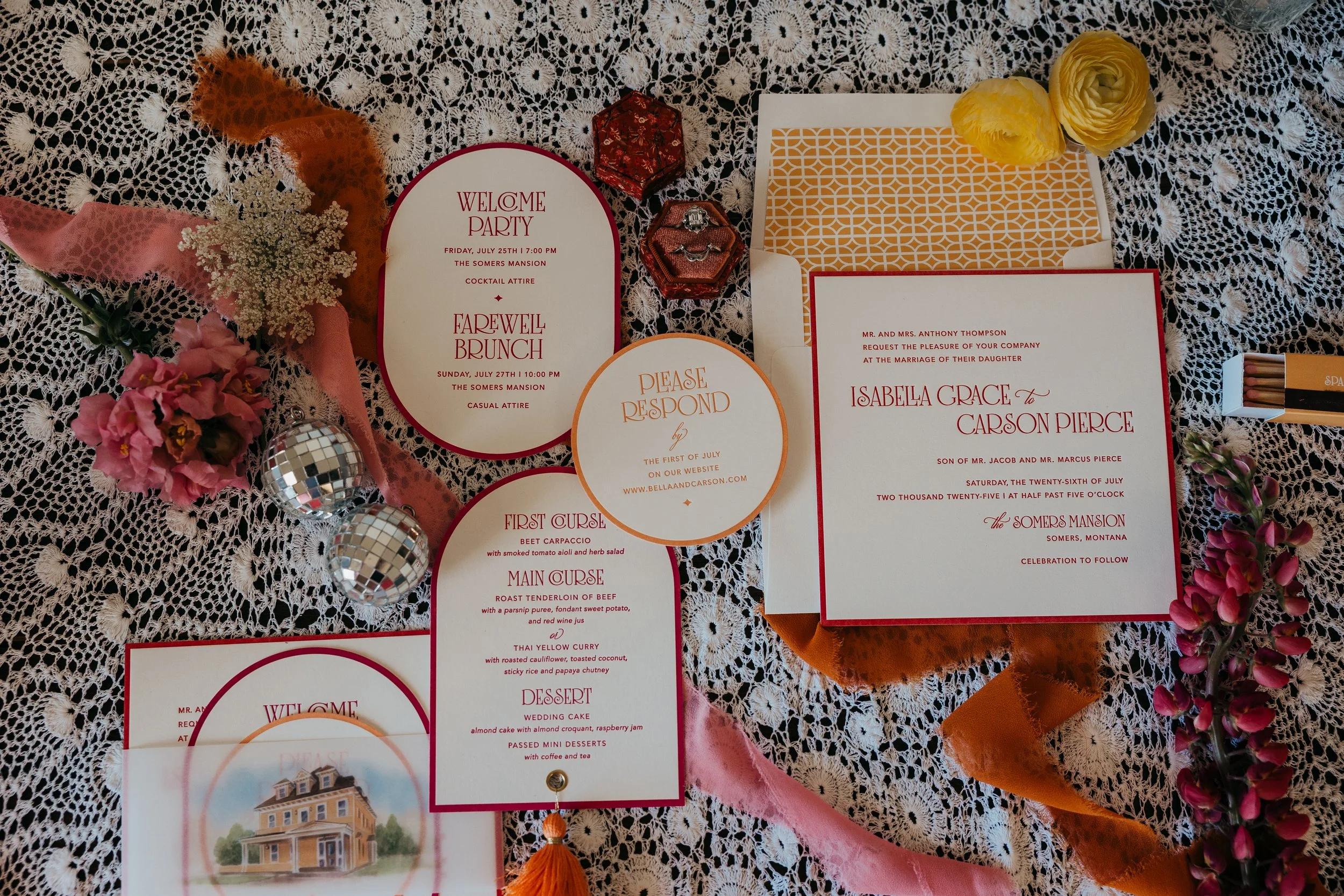 Wedding invitation suite on lace tablecloth, includes main invitation, RSVP card, schedule, menu, and RSVP envelope, surrounded by flowers, small disco balls, jewelry, and decorative boxes.