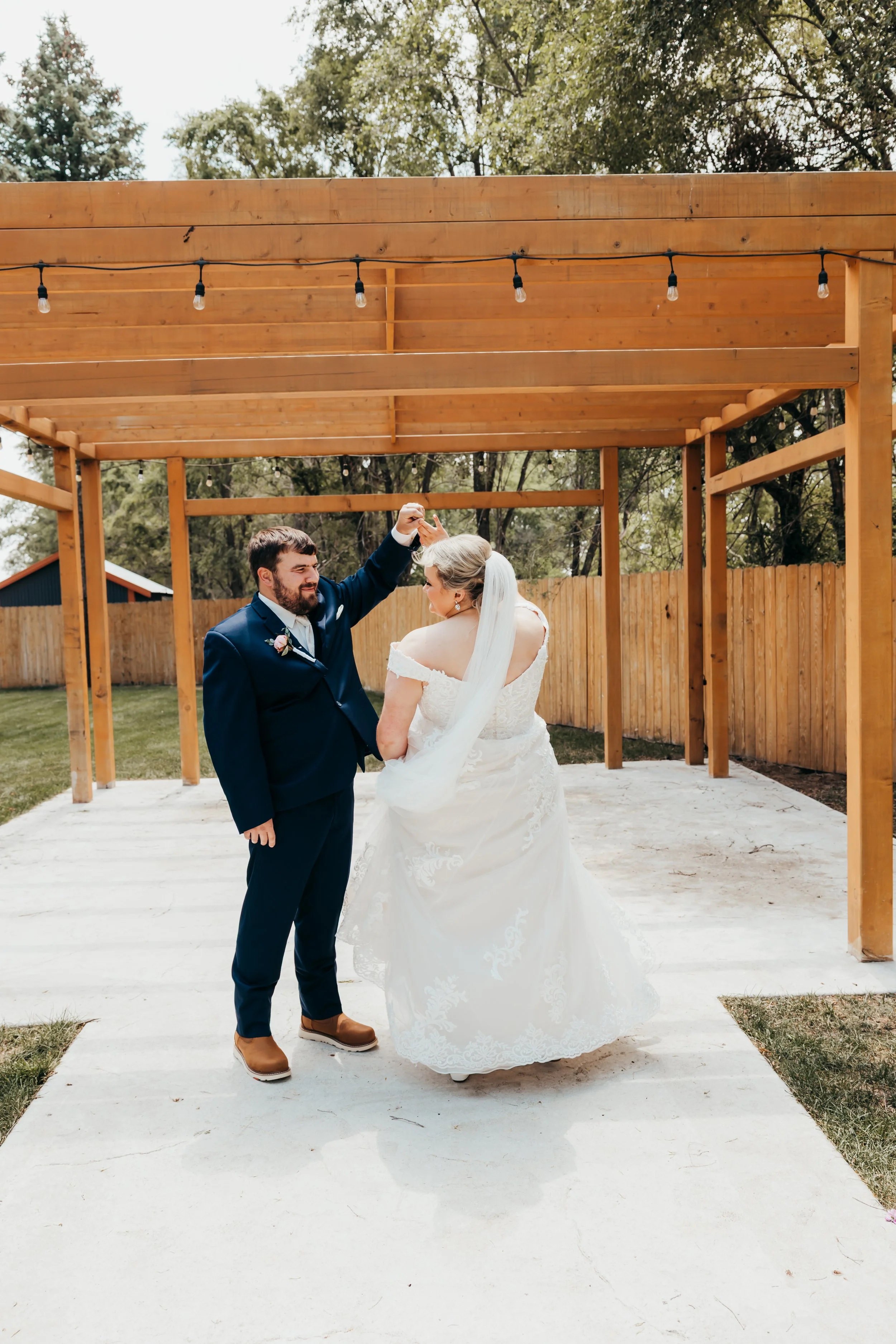 A bride and groom dancing outdoors under a wooden pergola during their wedding celebration.