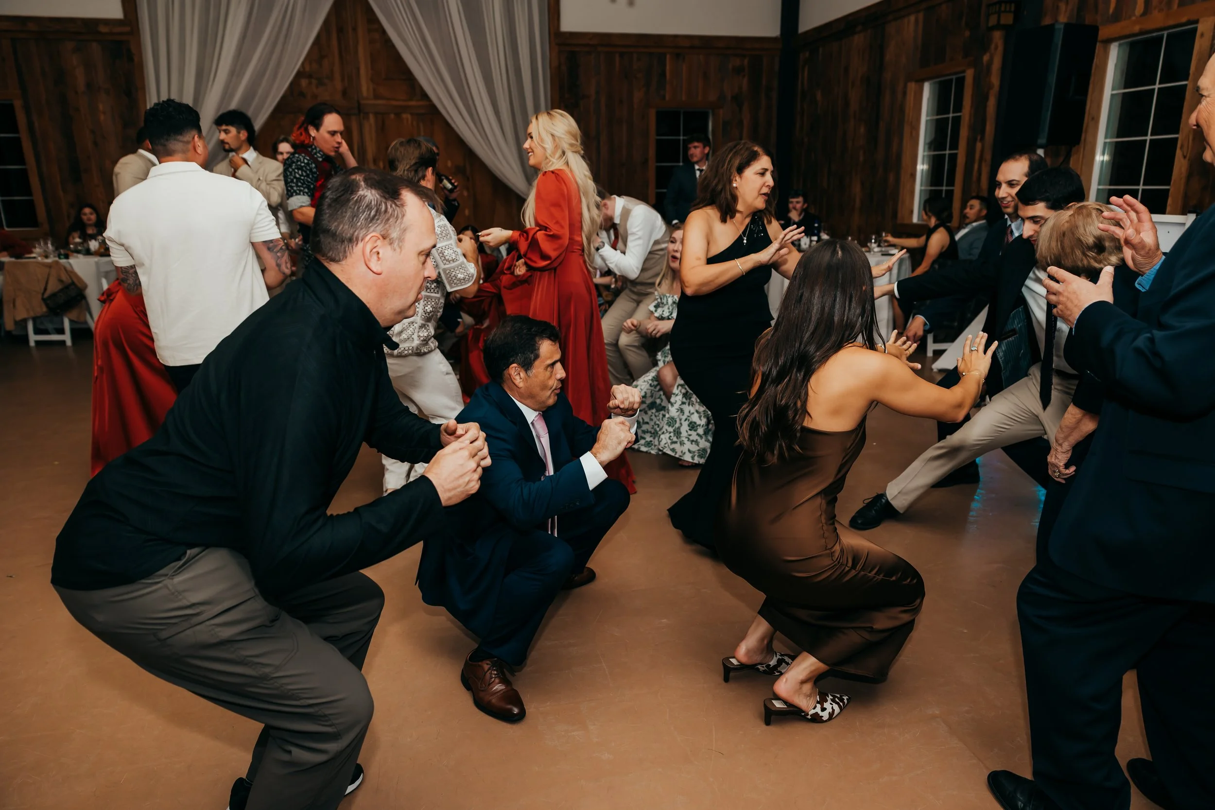 People dancing and having fun at a party or celebration in a wooden-finished room with decorative curtains.