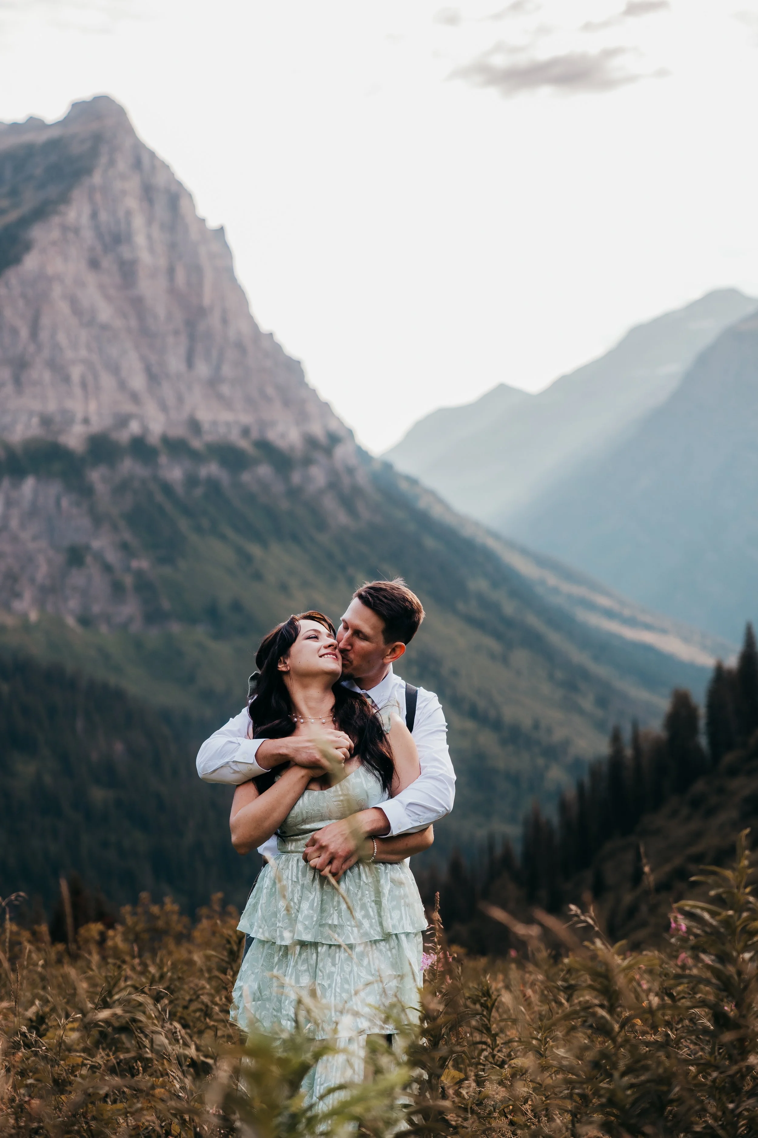 A couple embracing outdoors in a scenic mountainous landscape during daylight.