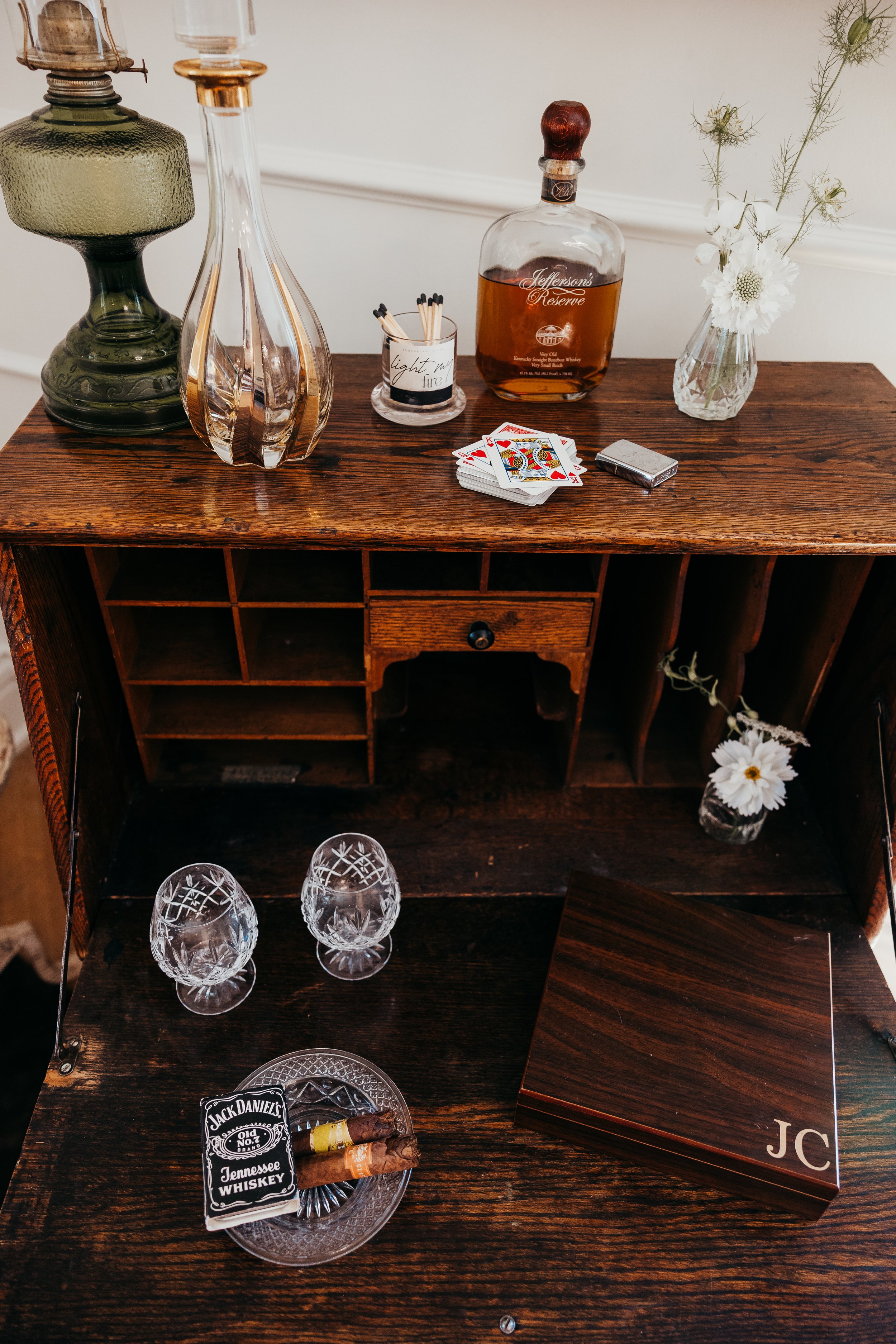 A vintage wooden bar cabinet with two glasses and cigars on a glass tray, and a box on the right side.