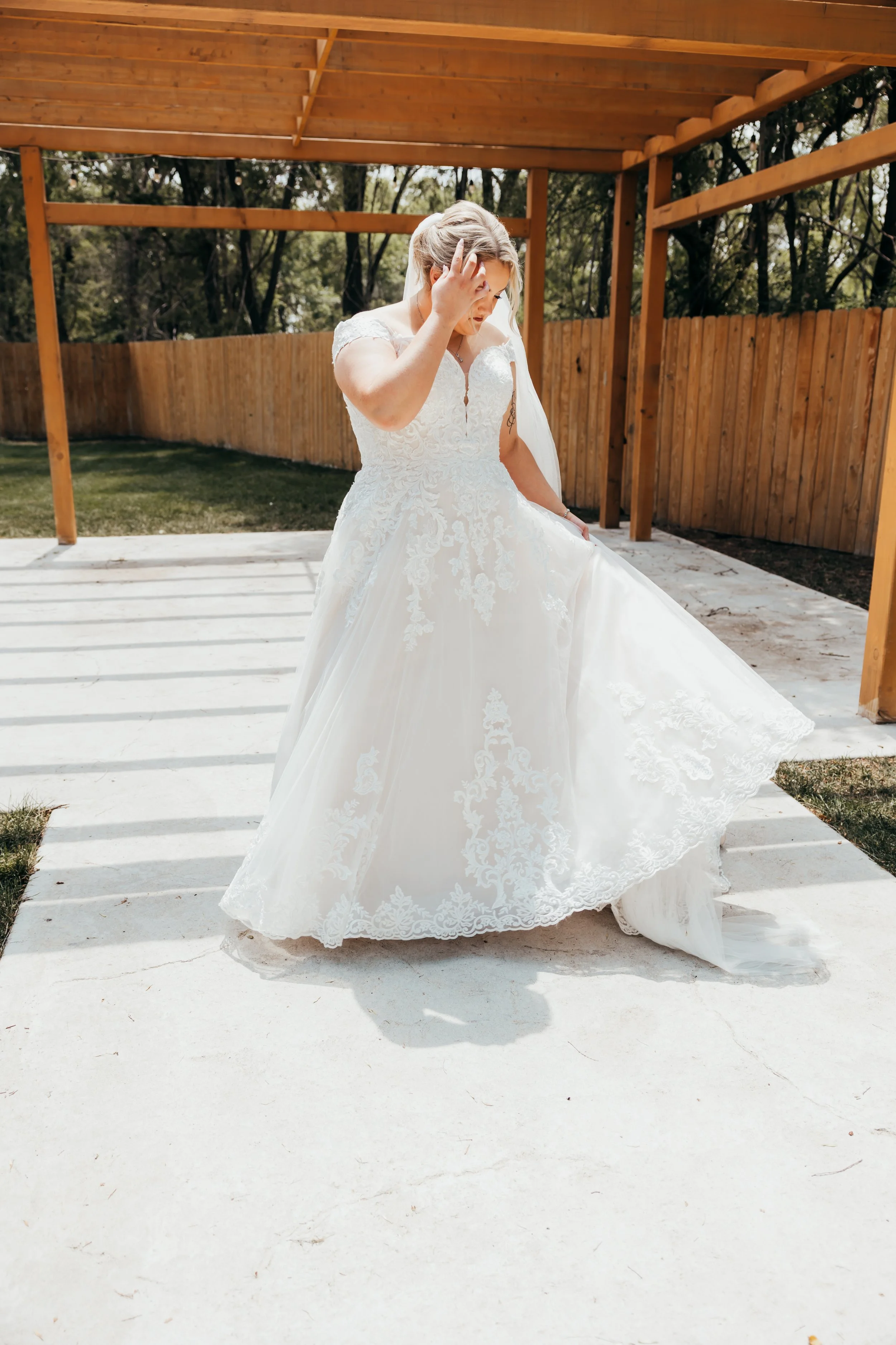 Bride in a white wedding dress adjusting her hair outdoors on a sunny day.