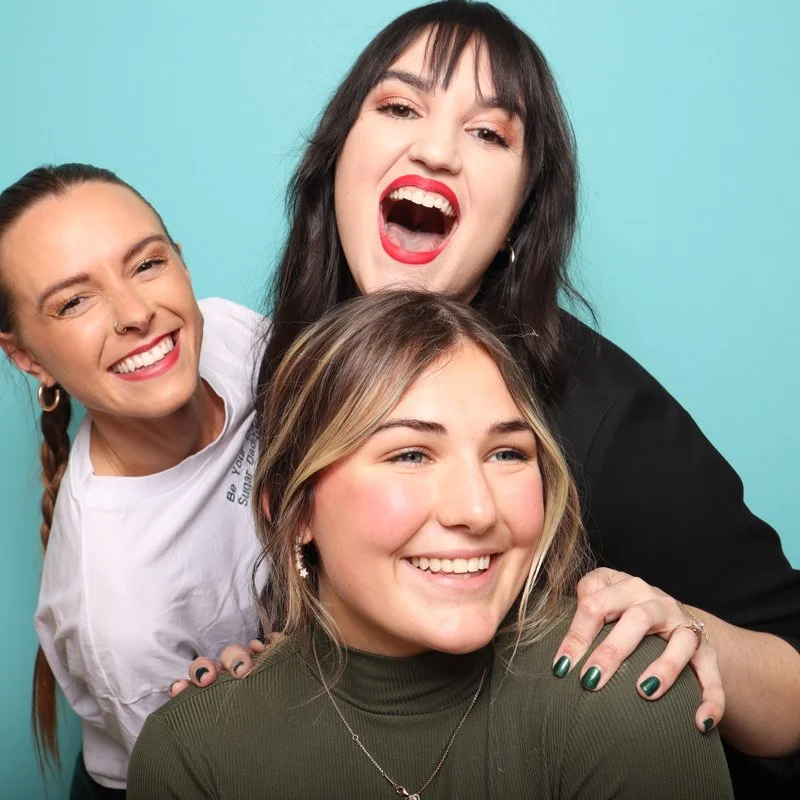 Three women in a photo booth with a blue background