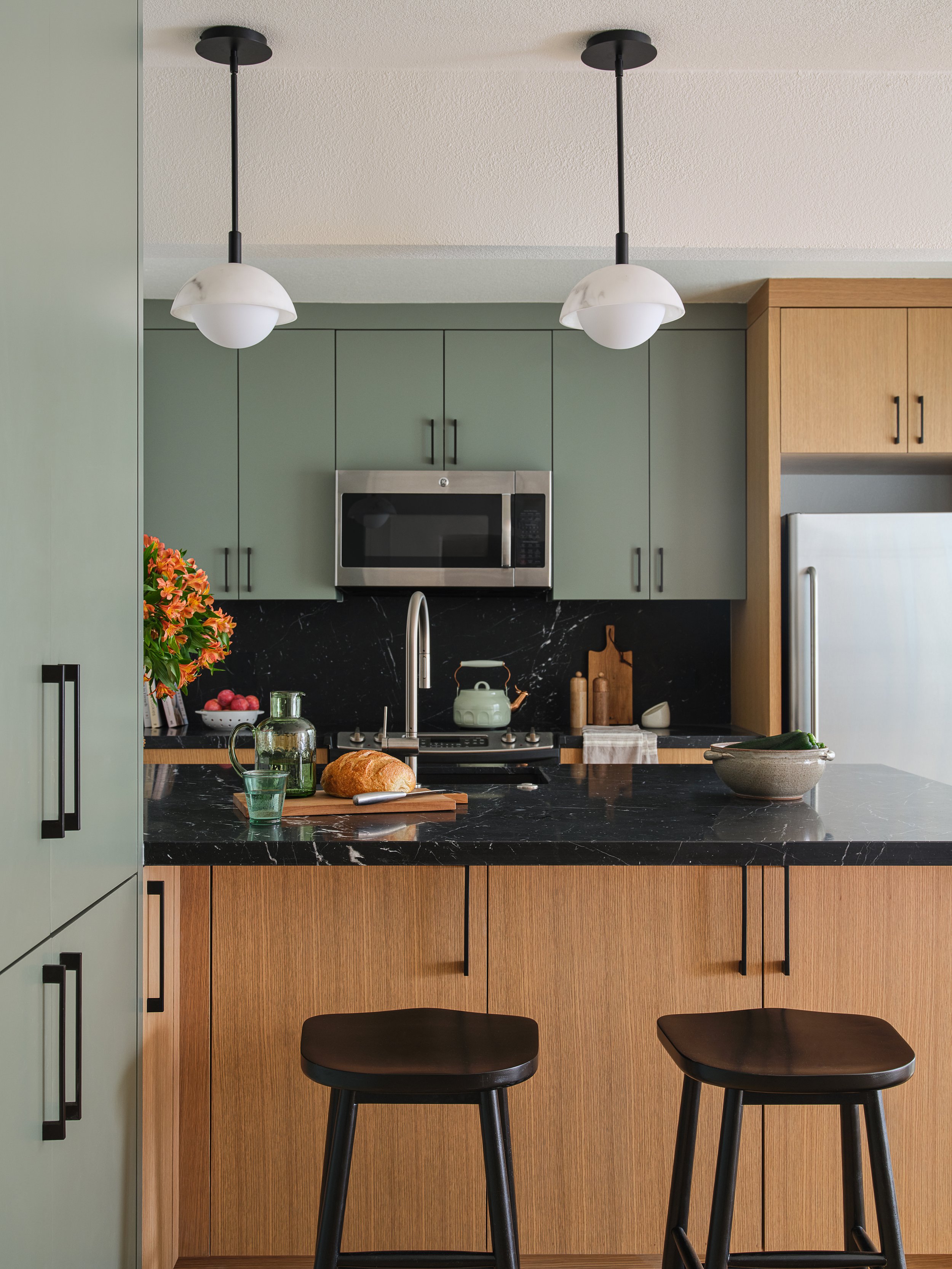 Residential kitchen bar with green cabinets, white oak, and black marble