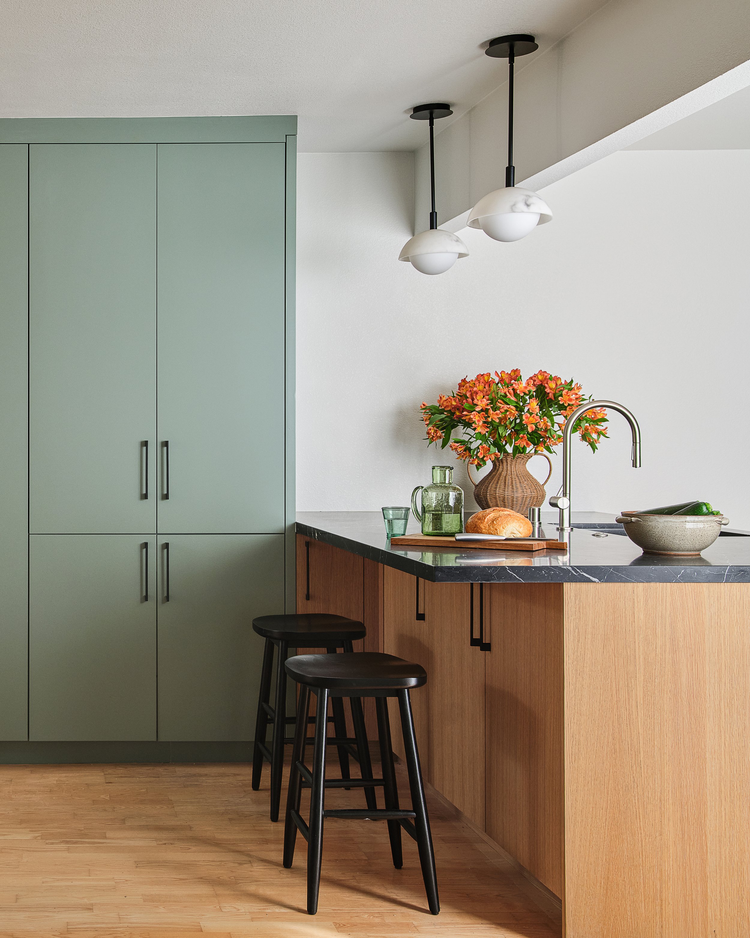 Residential kitchen bar with green cabinets, white oak, and black marble