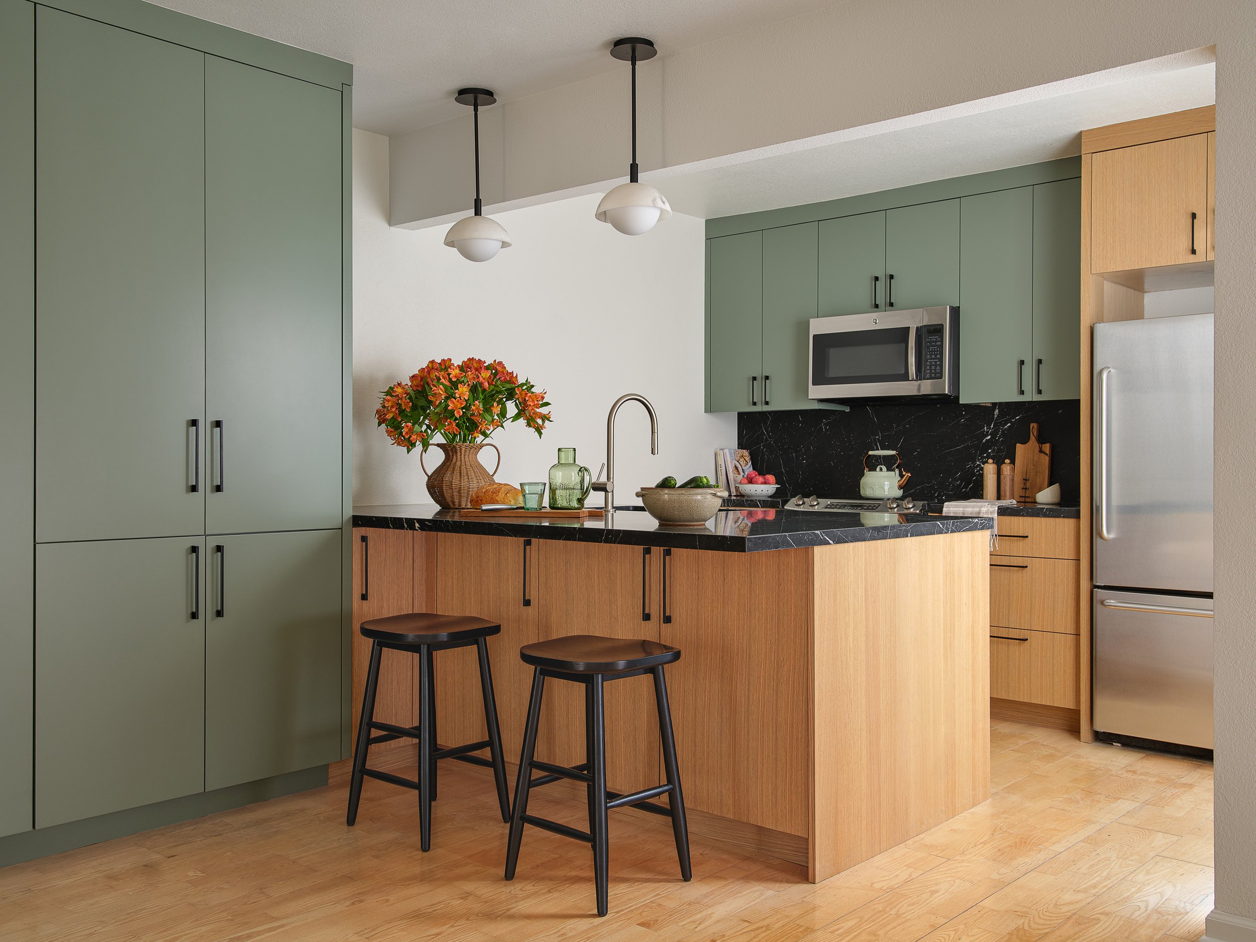 Residential kitchen bar with green cabinets, white oak, and black marble
