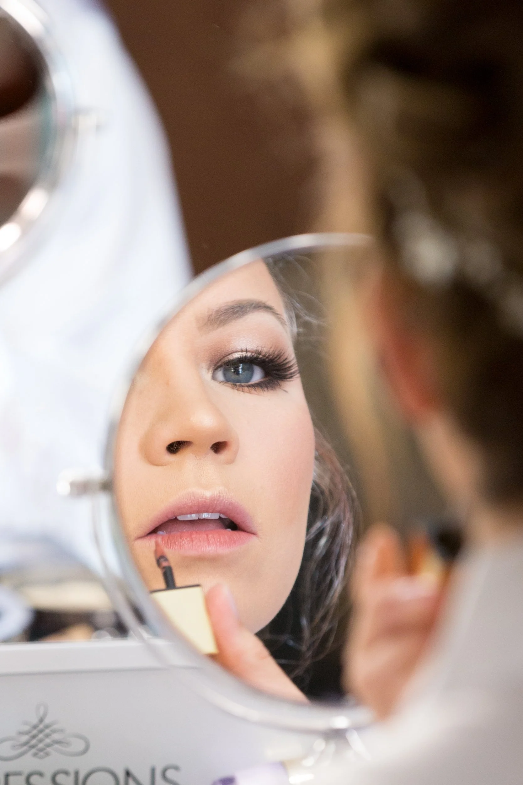 Bride applying makeup in front of the mirror.  