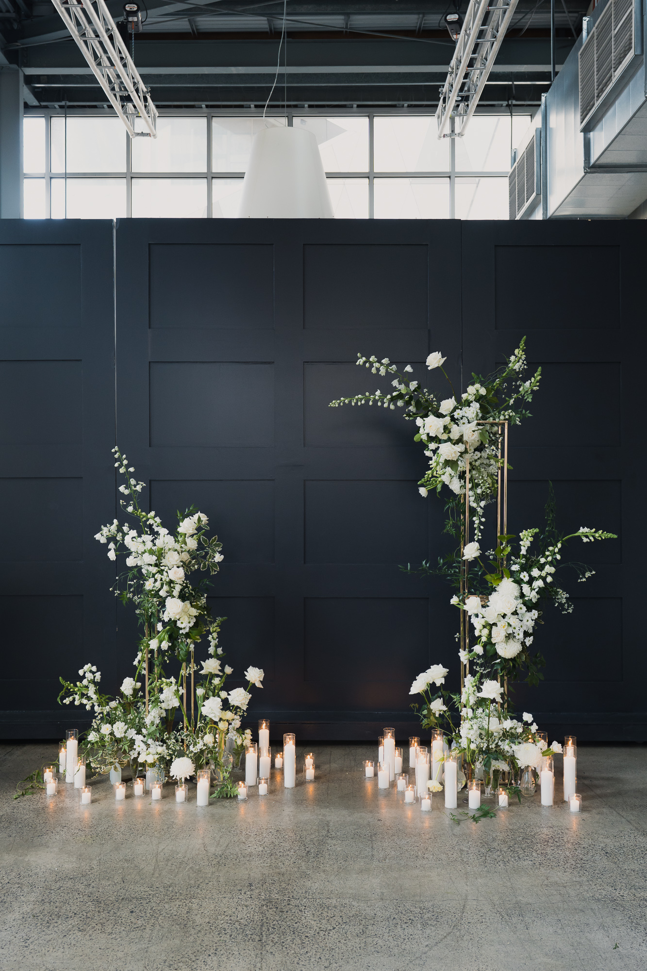 Elegant wedding backdrop with white floral arrangements and candles on the floor. Alto Event Space by Damn Fine Food Co.