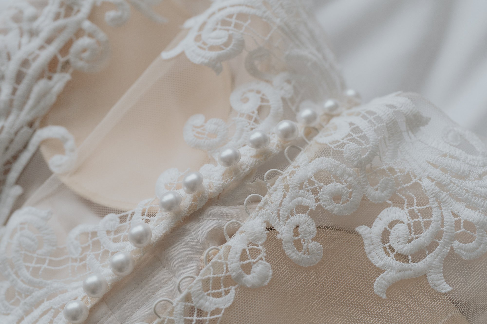 Close-up of white lace bridal gown with embroidery and pearl embellishments.