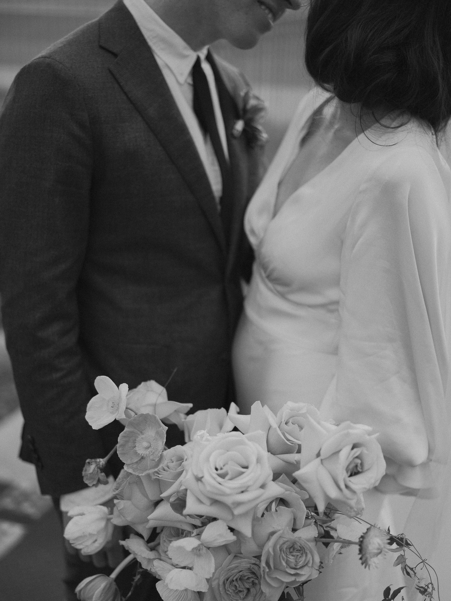 Black and white photo of a couple on their wedding day, standing close together, with the bride holding a large bouquet of roses and other flowers.