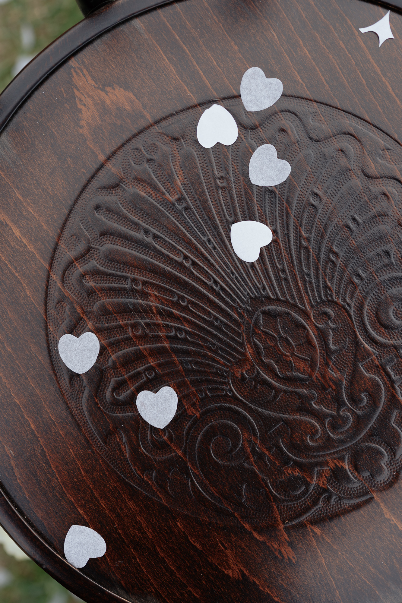 Heart-shaped confetti scattered on a dark, engraved wooden surface.