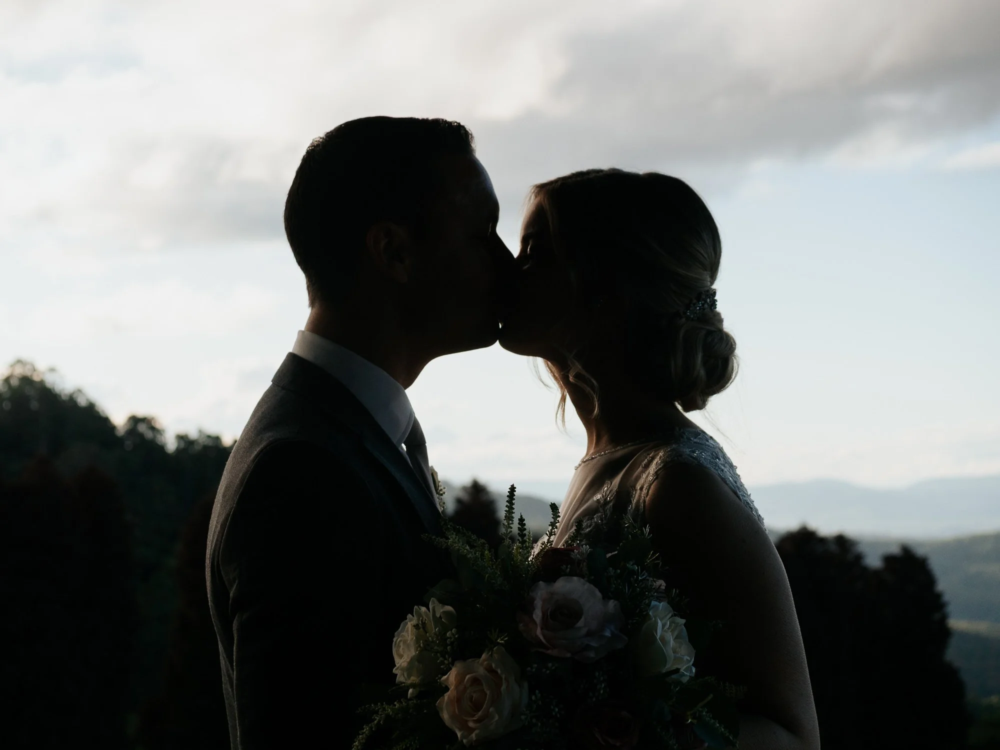 Silhouette of a bride and groom kissing outdoors at sunset.