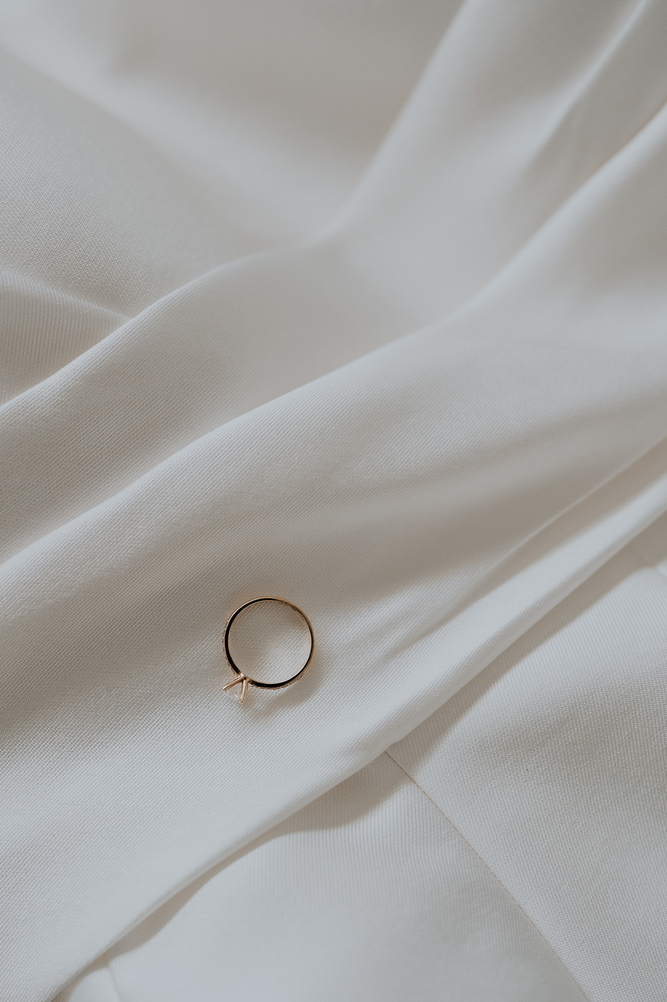 A close-up of a delicate ring with a small bow on a cream-colored fabric surface.